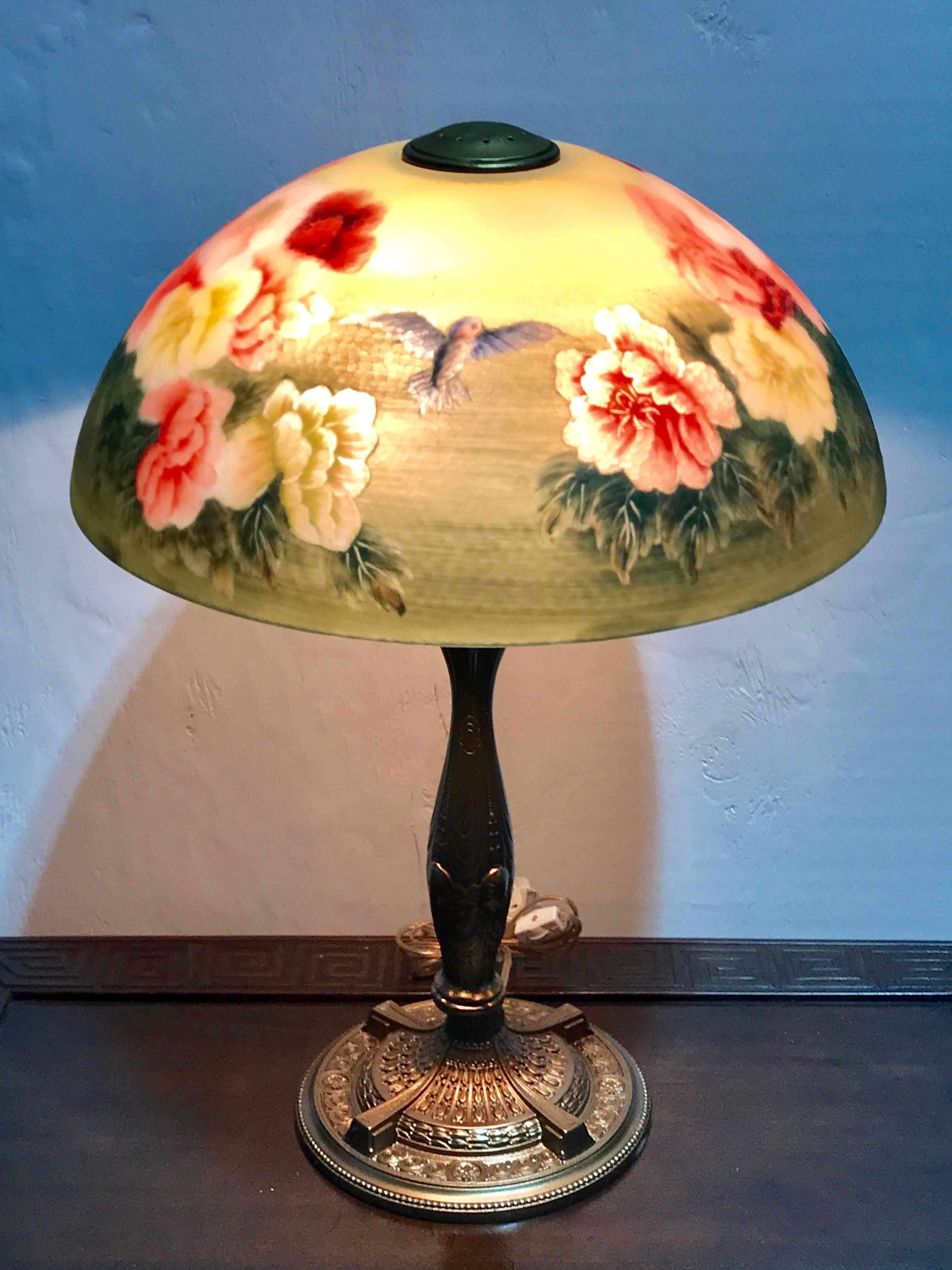 Handel style reverse painted table lamp birds and flower motif, painted with two birds at each side, flanked with lush cabbage roses. Raised on a newly rewired neoclassic enameled base. Unsigned. The diameter of the base is 7 inches.
