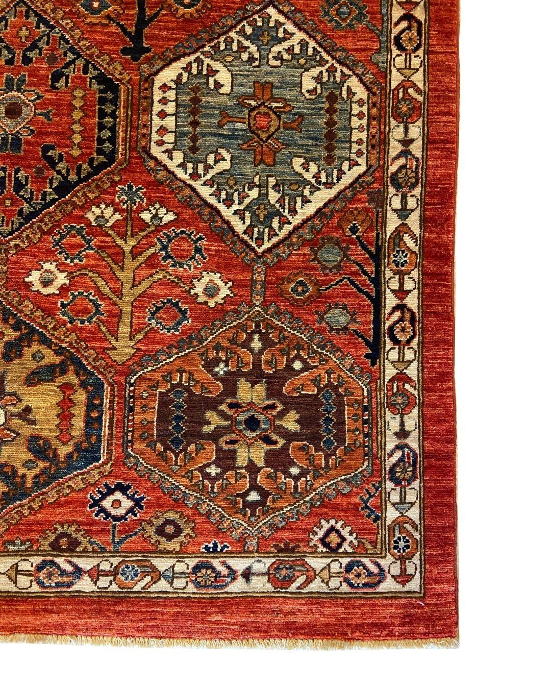This hand-knotted geometric wool rug measuring 4' x 6' is a striking example of tribal design, blending traditional medallions with a bold, contemporary sensibility in red, blue, and gold. The richly saturated field is adorned with a lattice of