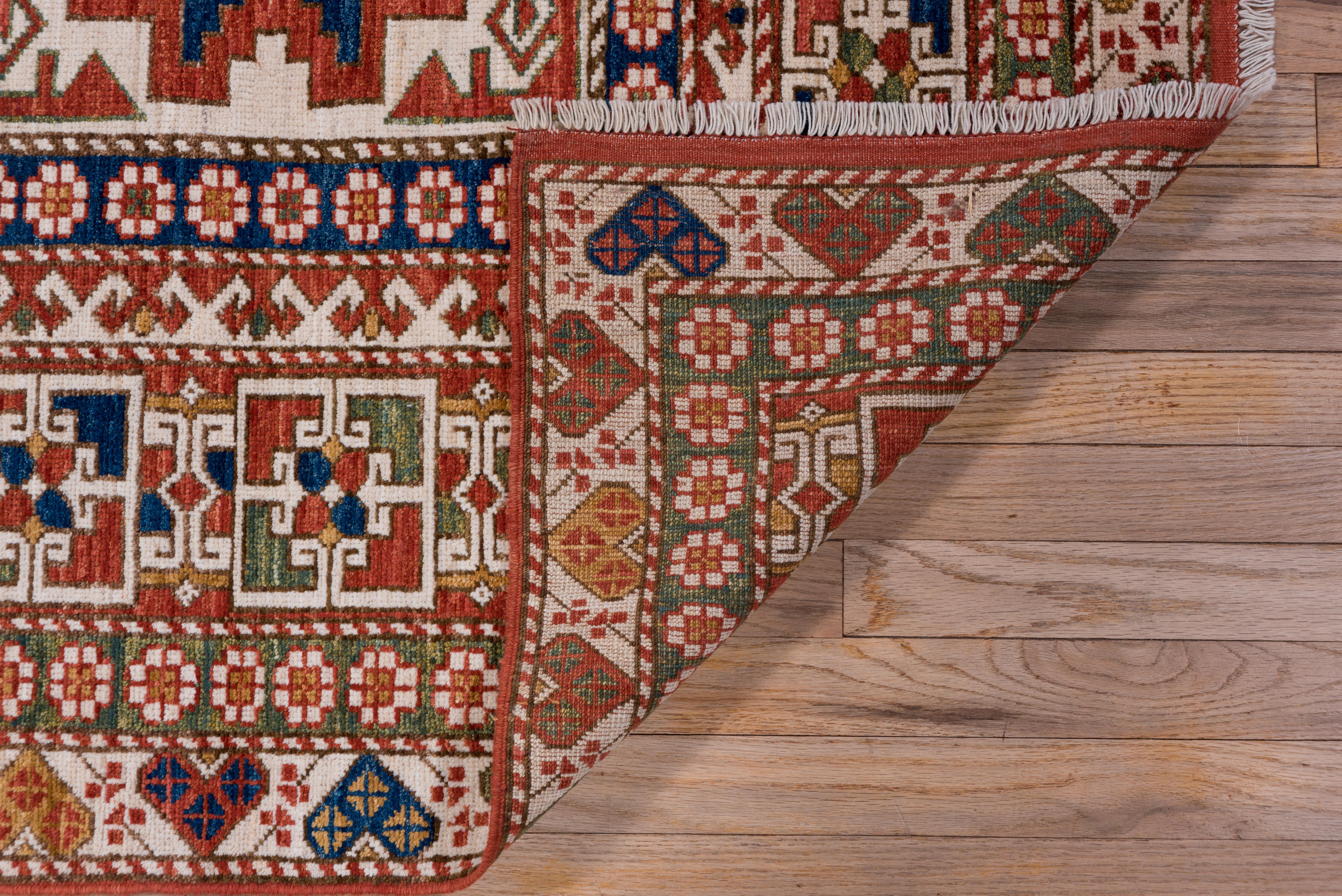 This modern Caucasian scatter shows a three-panel ivory field decorated by red and green 