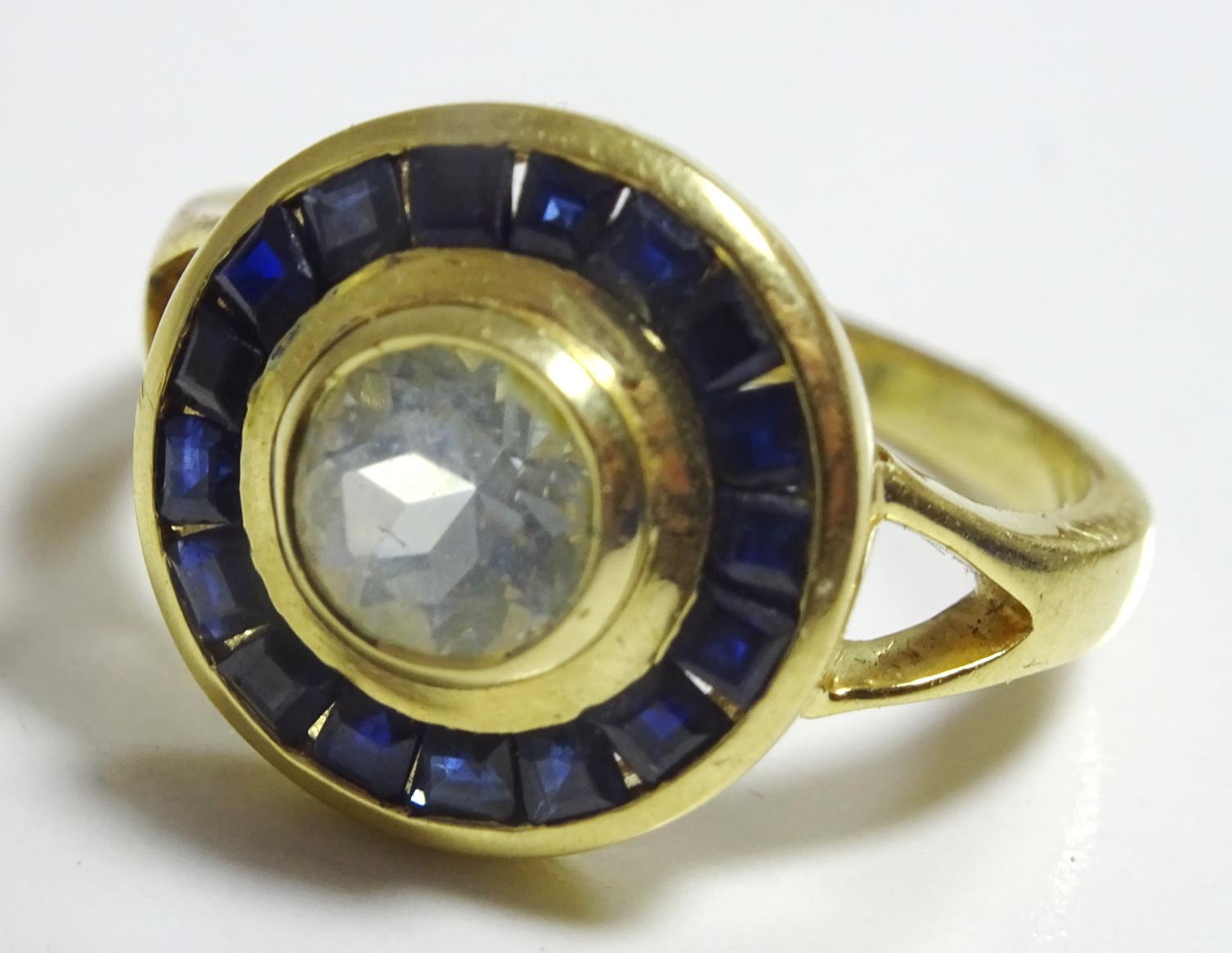 A Beautiful Handcrafted Ring made in 18 karat Gold ( there is a clear hallmark ) The Centre stone is a 8 mm round pale blue Aquamarine weighing 1.5 carats. This stone is surronded by 20 2 mm square Sapphires in a channel setting, total carat weight