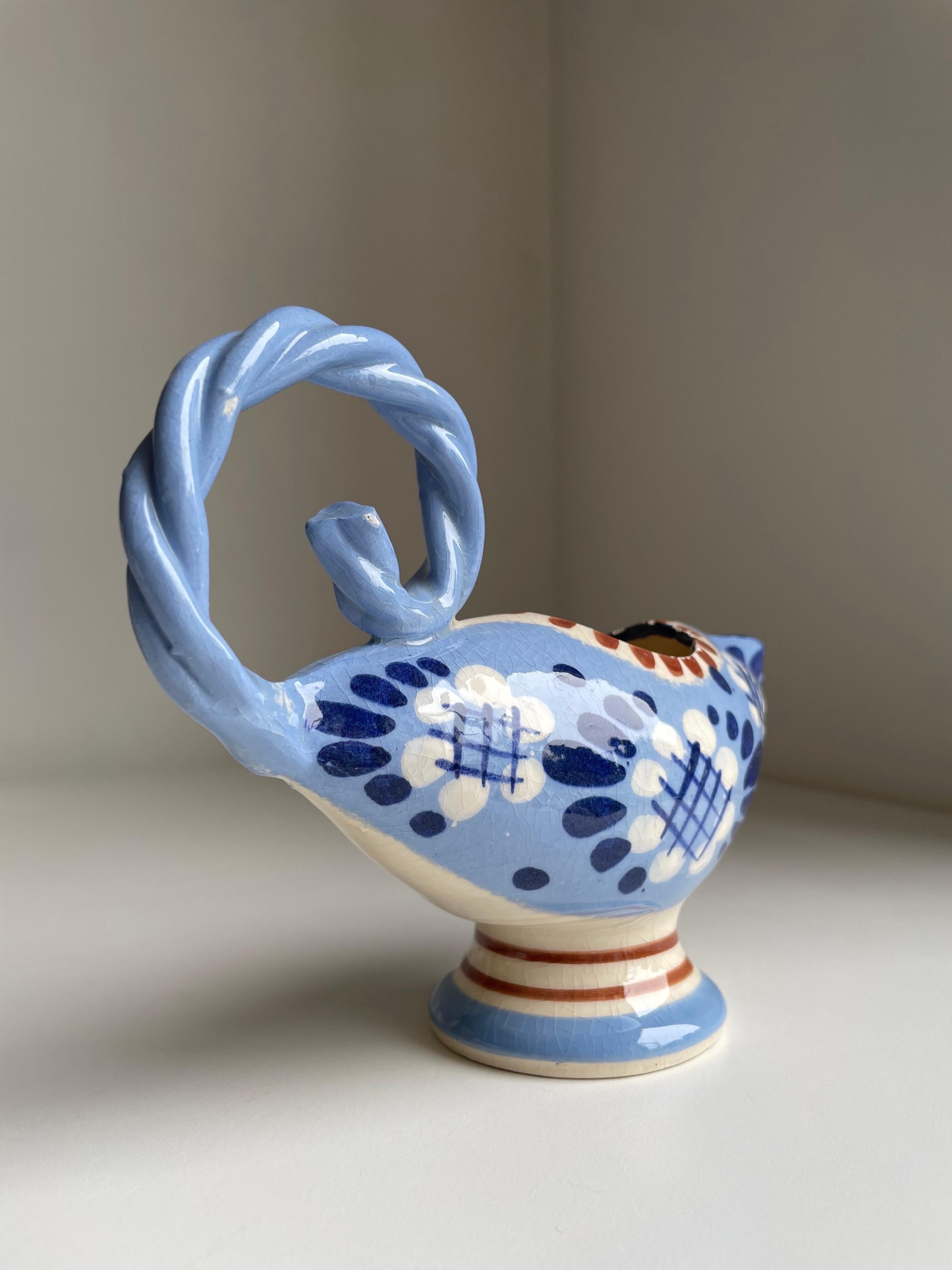 Handmade 1950s ceramic low pitcher vase with large braided handle. Light blue base with cream white and dark blue floral decor and cinnamon brown accents and lines. Stamped under base. Great vintage condition consistent with age and wear.
Denmark,