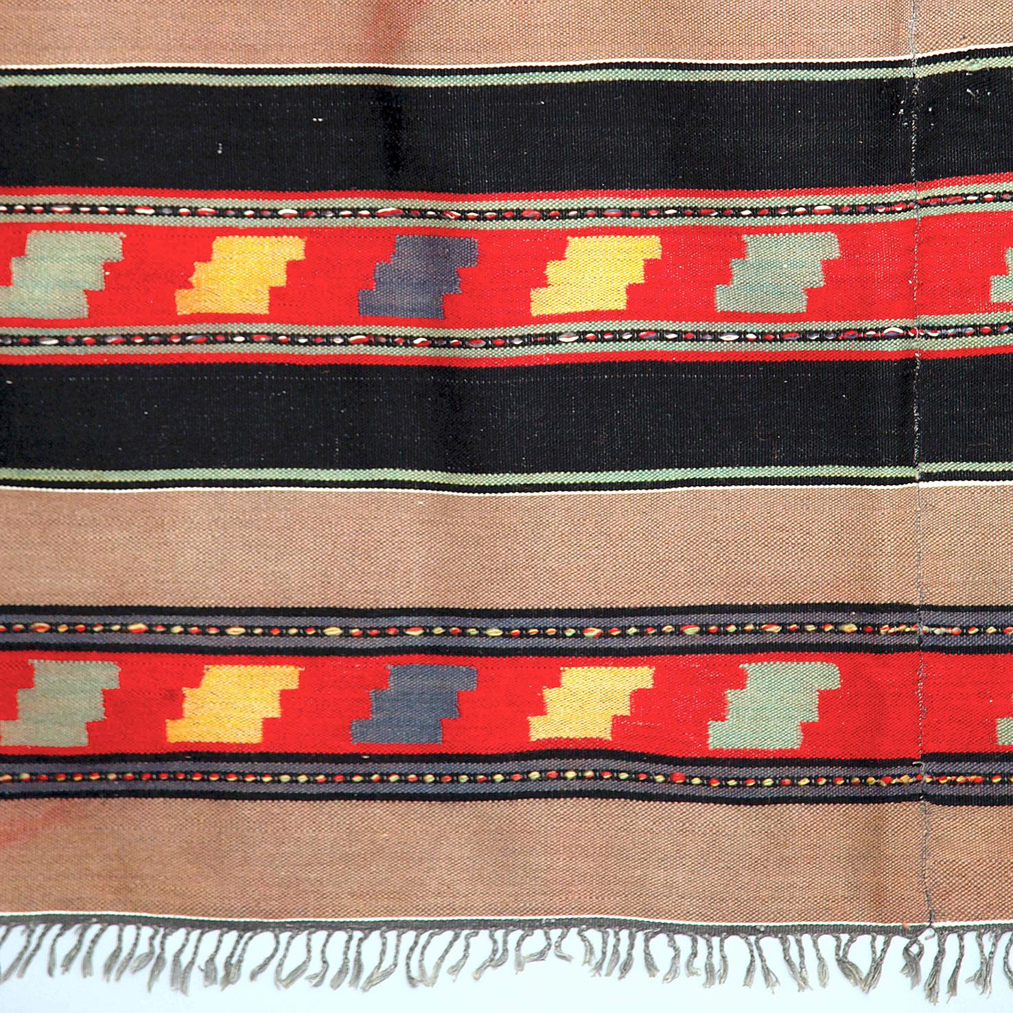 Ein handgefertigter Wollteppich in Schwarz und Braun, sowohl mit Streifen als auch mit geometrischen Mustern.
Dieser Teppich hat ein auffälliges Muster in Rot-, Gelb-, Blau- und Grüntönen, und obwohl er im Vintage-Look gehalten ist, lässt er sich