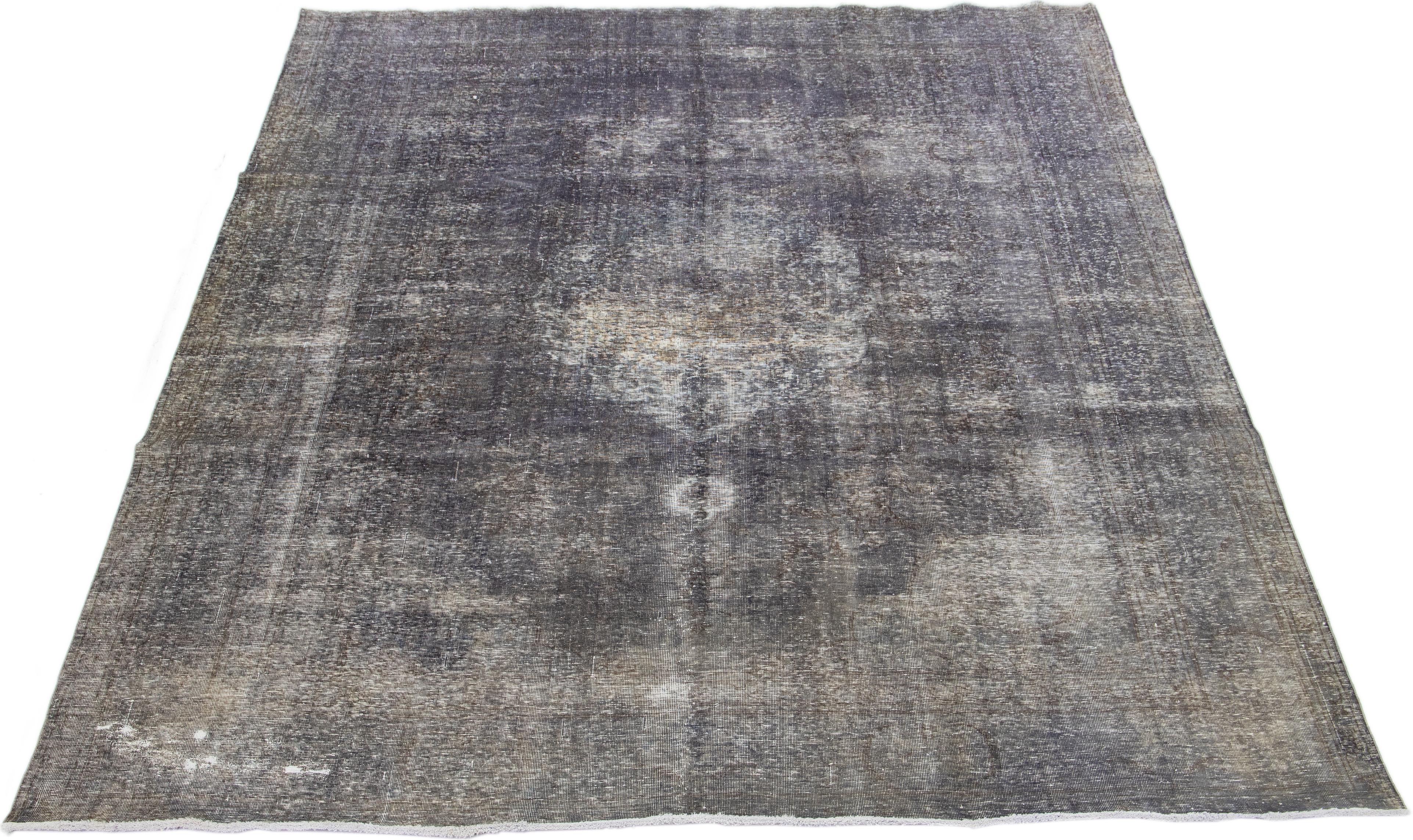 This Persian rug, originating from the 1960s, features an intricate floral design in shades of brown that has been intentionally distressed and dyed, resulting in a delightful rustic aesthetic. The rug's exceptional gray color exudes an aura of