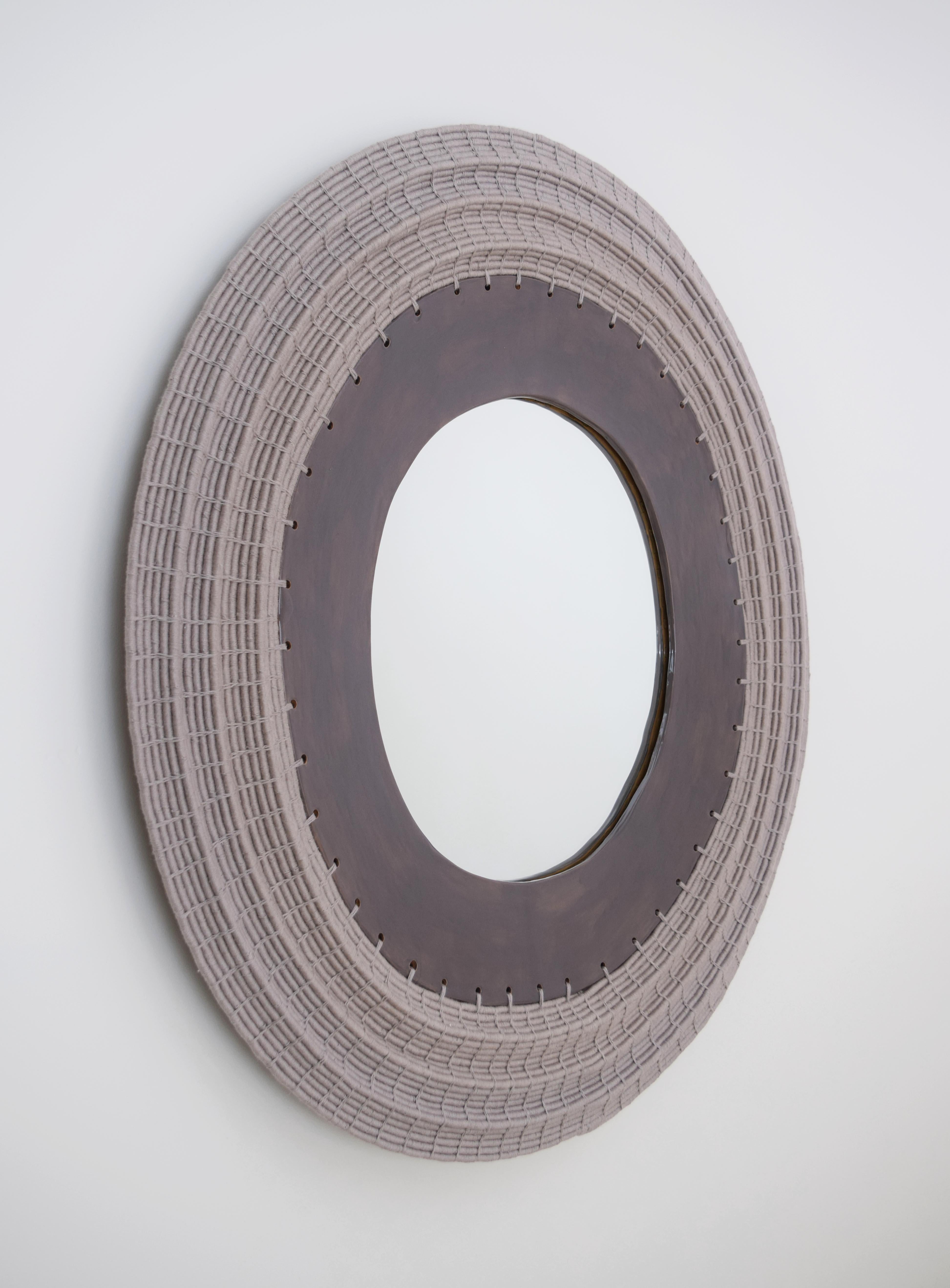 Made to order, and perfect for hanging in an entryway or in a powder room, this decorative mirror features a woven frame with an undulating, dimensional effect.

Hand formed stoneware frame. Woven cotton exterior frame. Black felt backing, hanging