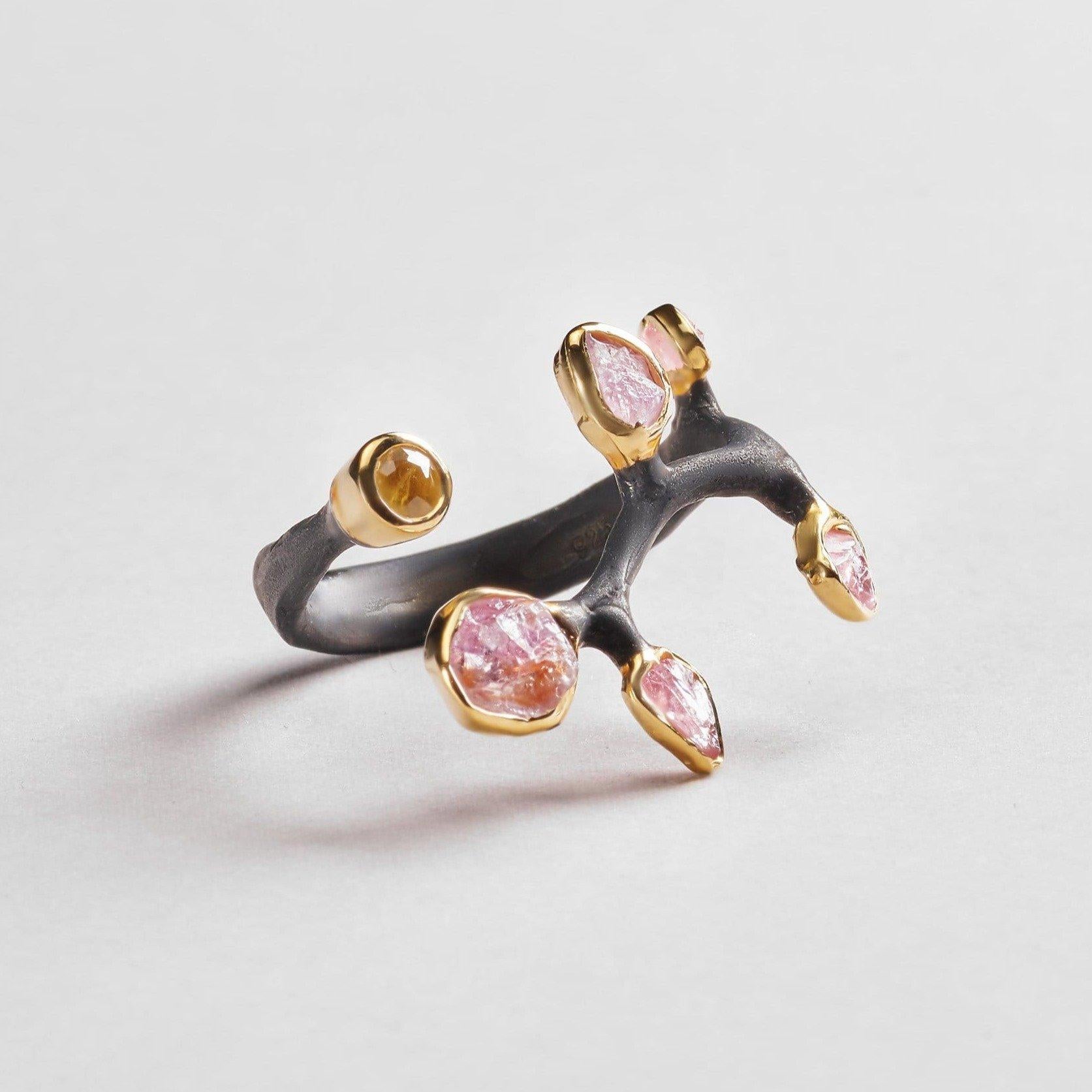 A beautiful black anthracite ring loops round in a natural sinuous curve and is dotted with sparkling yellow sapphires and rough spinel gemstones. Each has echoes of natural organic shape and form that is celebrated in true beauty.
