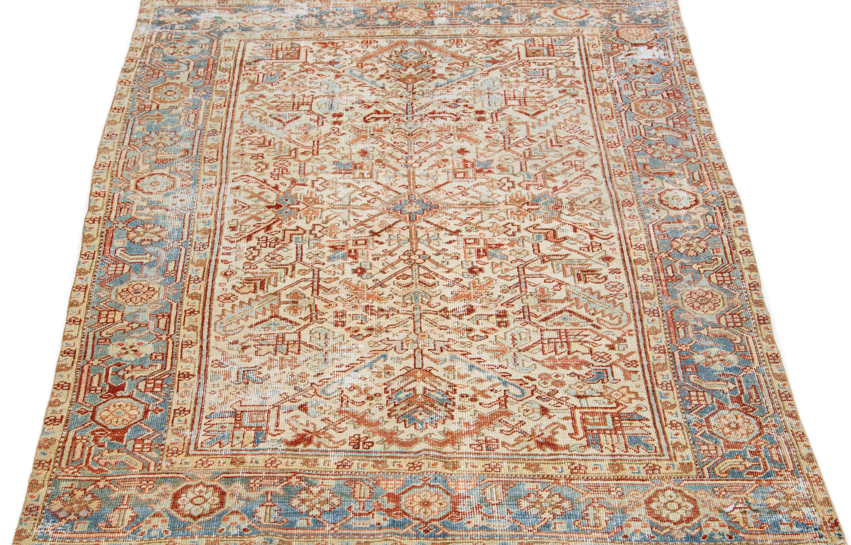 The antique Heriz rug exudes timeless elegance and sophistication with its premium hand-knotted wool and striking all-over design. The eye-catching geometric floral pattern in shades of blue and rust adds a touch of allure to the soft beige field,