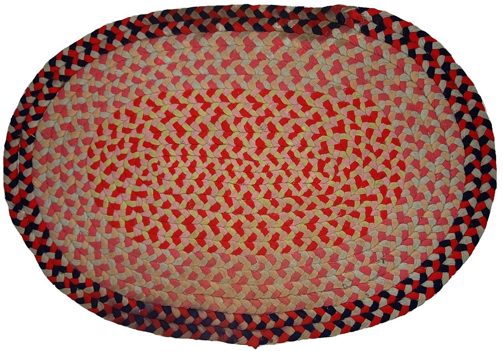 Antique handmade American Braided rug in oval shape. The rug made in cotton in red, navy and yellow shades. It has some age discolouration’s.
 