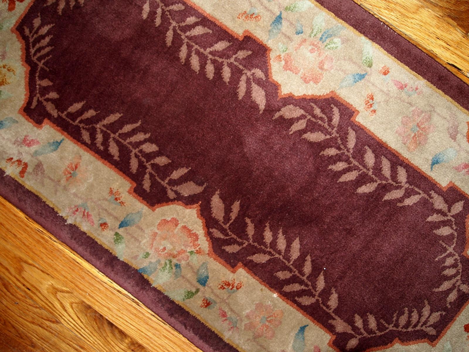 Tapis chinois Art Déco bordeaux avec une belle bordure florale claire. Les feuillages entourent le champ comme deuxième bordure. La bordure crème claire est couverte de branches pleines de fleurs colorées.