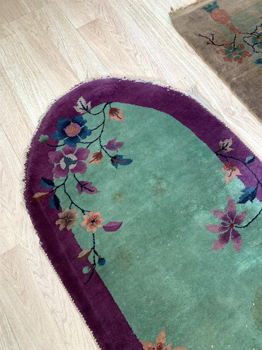 This antique Chinese Art Deco rug from the 1920s showcases an elegant oval shape and vibrant floral motifs, embodying the bold and colorful style of the Art Deco era. Its petite size and timeless design make it a versatile accent piece for any