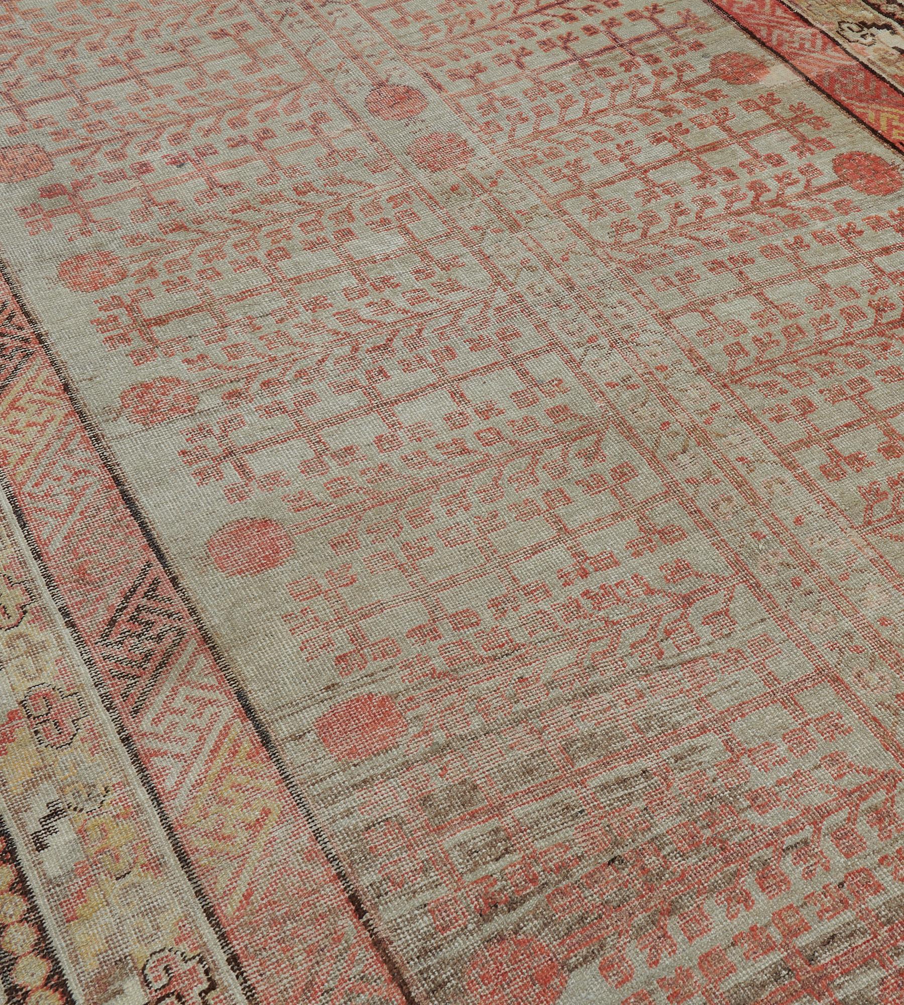 Dieser antike Khotan-Teppich aus der Zeit um 1880 hat ein Eau-de-Nil-Feld mit einem Gesamtmuster aus einer hellen, terrakottaroten vertikalen Tafel, die ein zentrales Stangenmotiv enthält, das von einer kleinen Vase ausgeht, eine zarte Blumenranke,