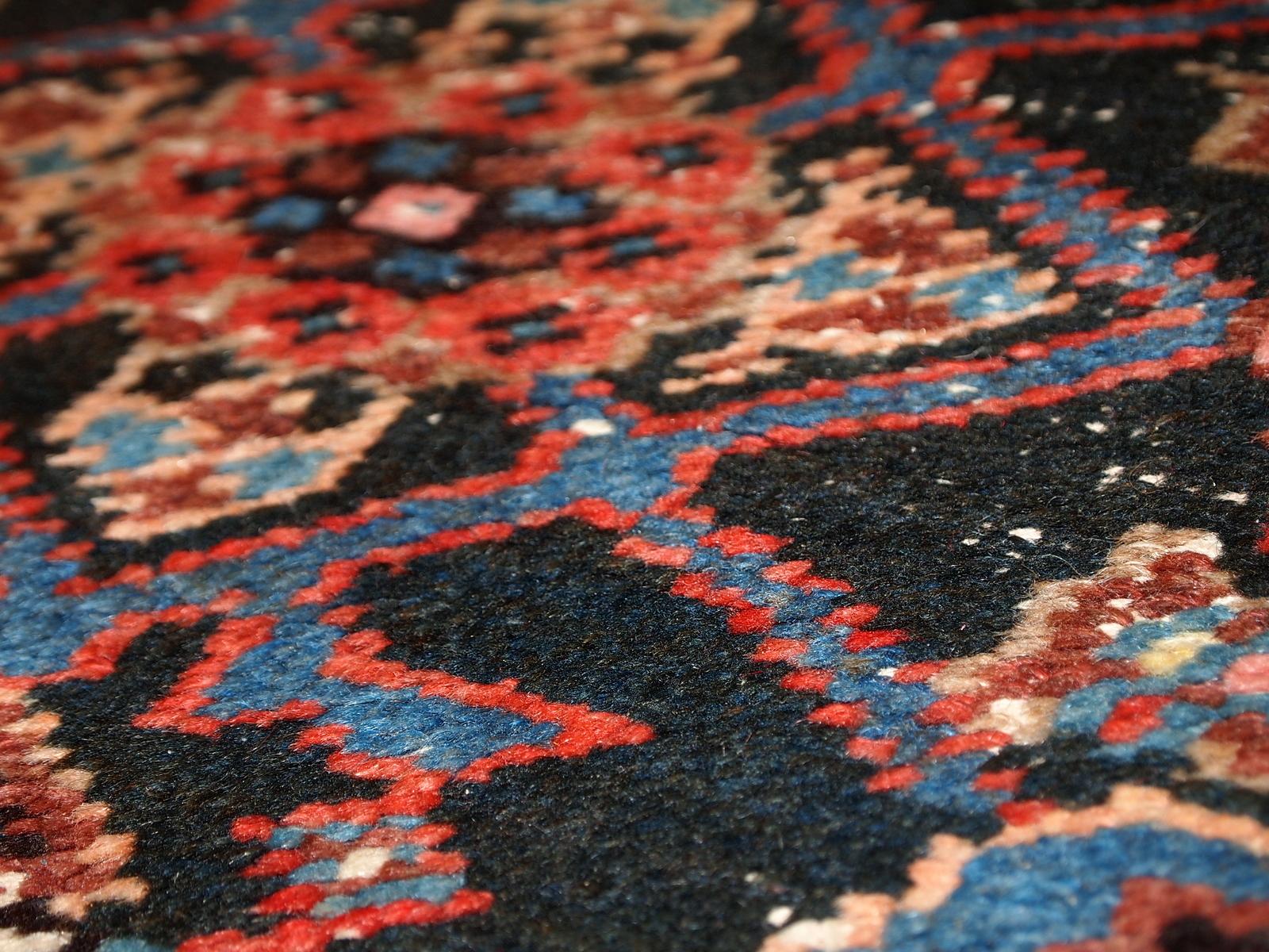 Handmade antique Persian Hamadan runner in original condition with some age wear. There no holes on the rug, just some low pile in certaine spots. The background is black, tribal design in blue and red. The runner is unusually narrow for its