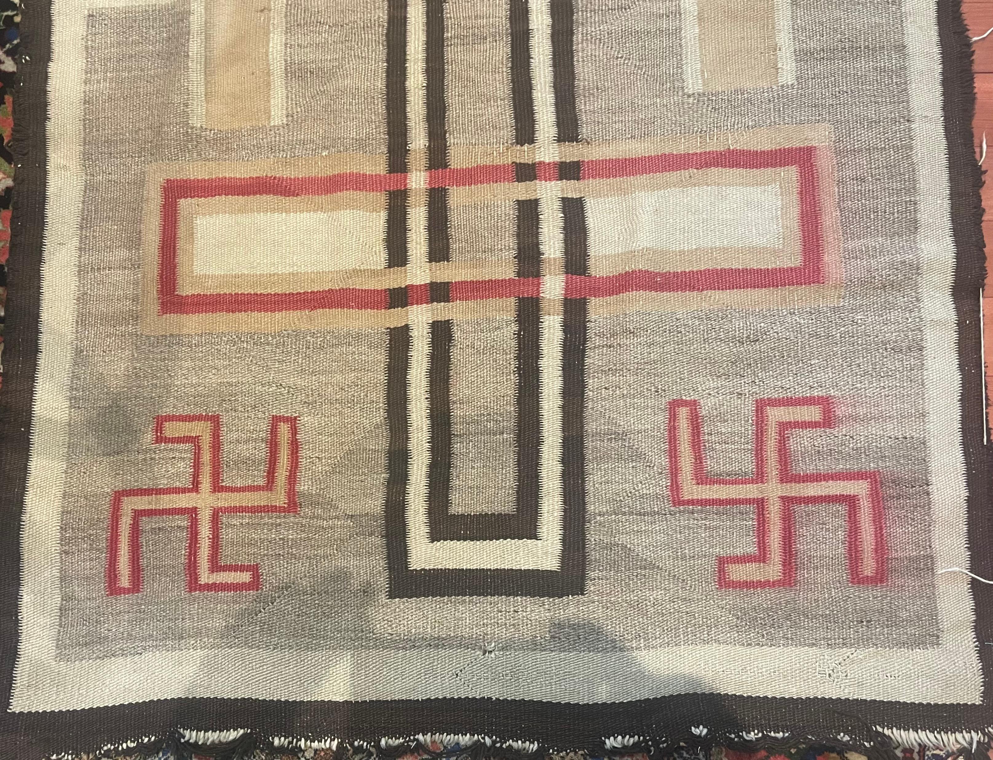 Ce tapis Navajo ancien, fait à la main et mesurant 115 cm sur 185 cm, est un magnifique exemple de l'artisanat traditionnel du début des années 1900. Fabriqué entièrement en laine, ce magnifique tapis présente des motifs complexes et une riche