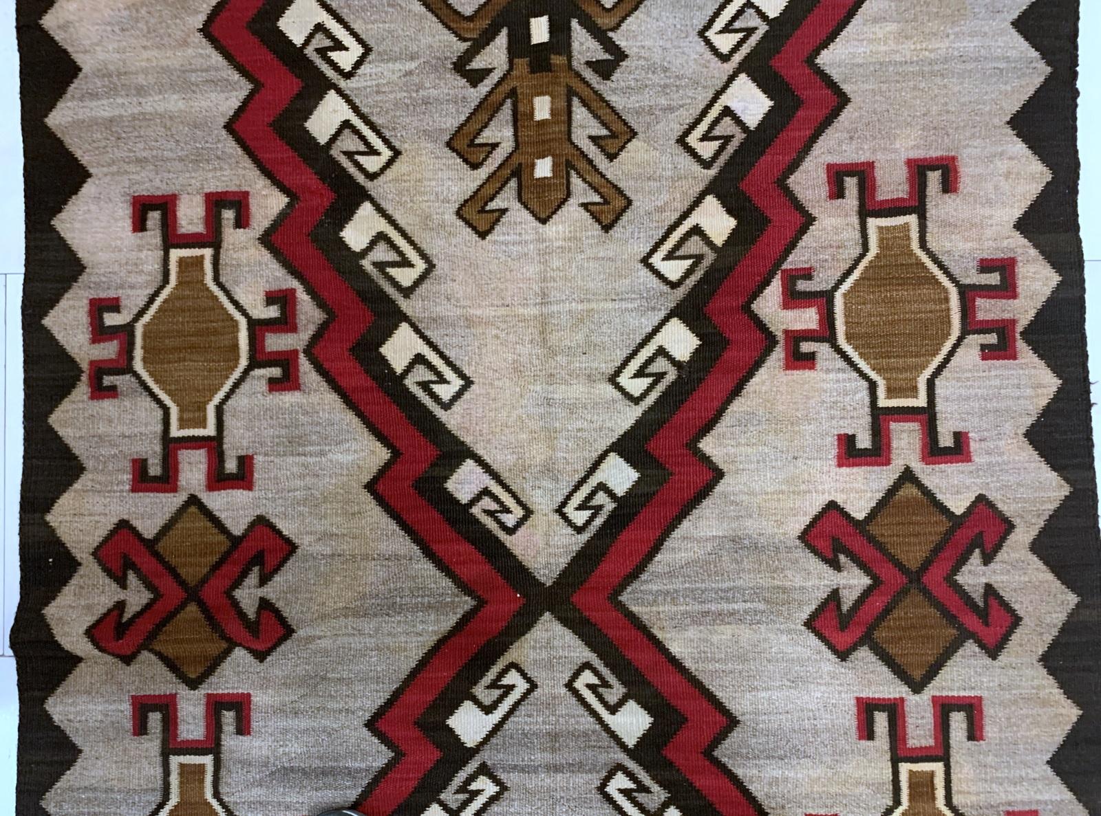Experience the artistry and heritage of Native American weaving with this handmade antique Navajo wool rug from 1910. Measuring 4.3 ft x 6.3 ft (131 cm x 192 cm), this rug showcases intricate geometric patterns in rich hues of red, brown, black, and