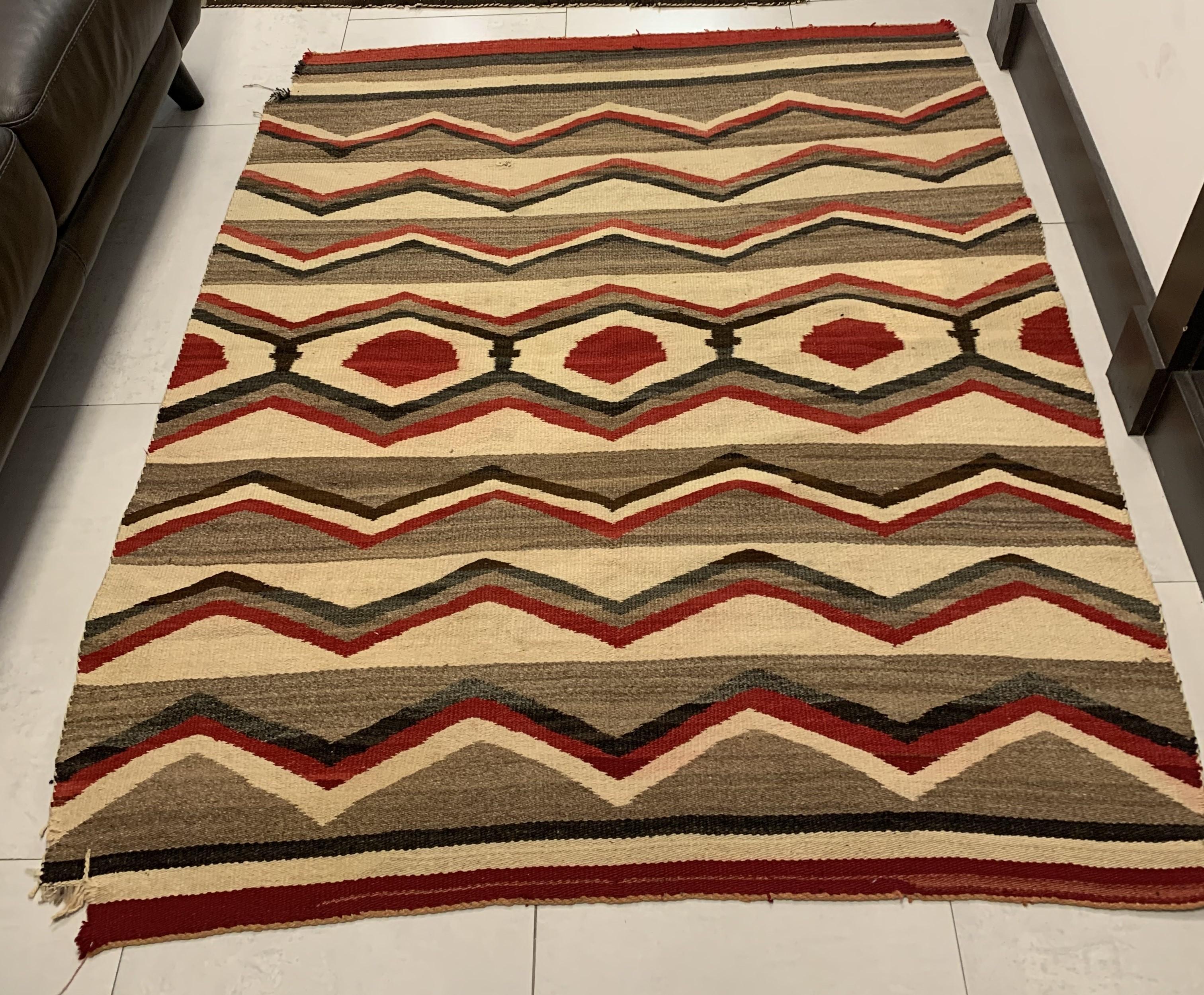 Nous vous présentons notre couverture de tapis Navajo antique fait main, une pièce captivante chargée d'histoire. Mesurant 4,6' x 5,4' (140cm x 164cm), ce tapis du début des années 1900 porte les marques du temps, notamment un coin