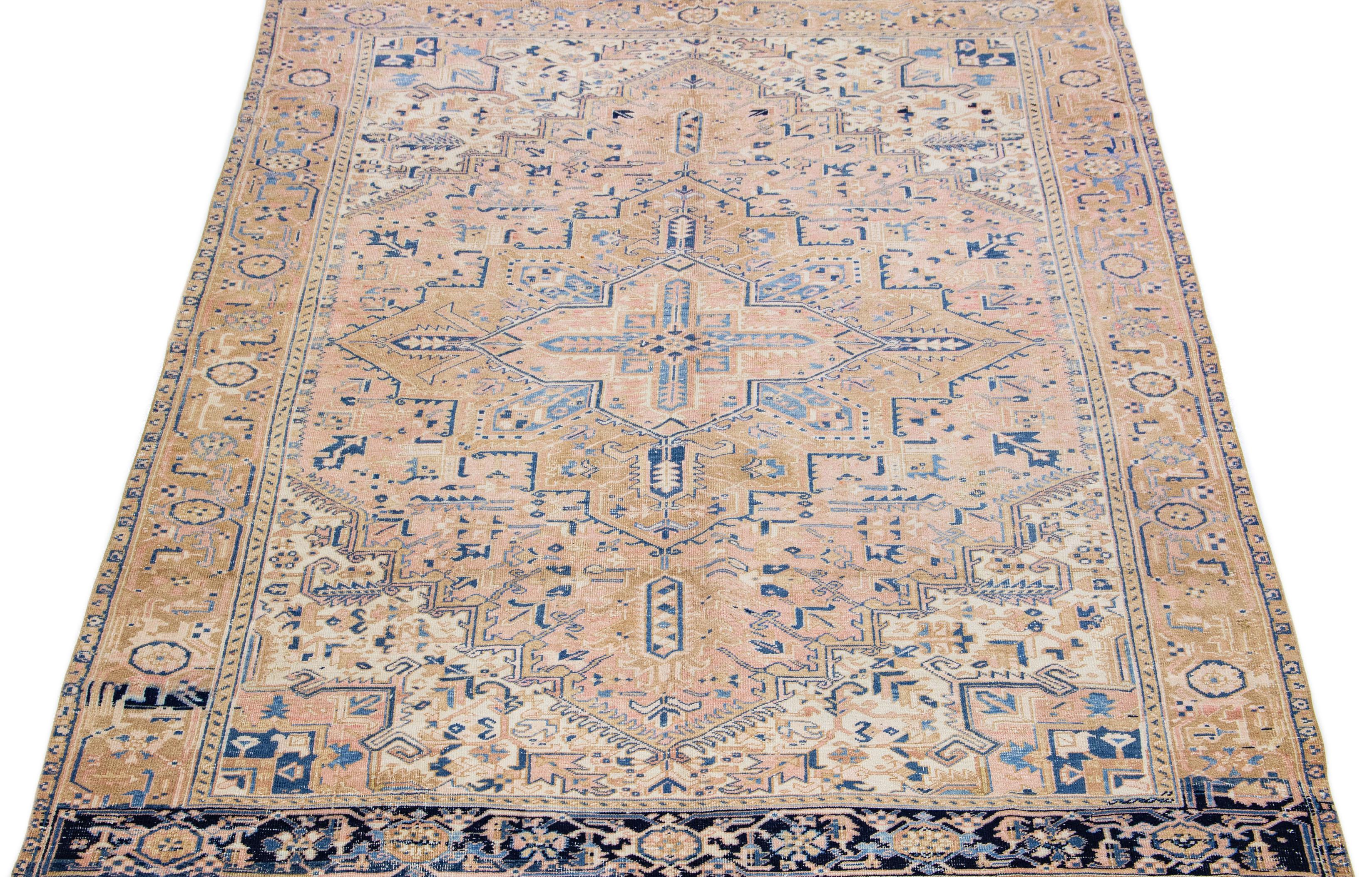 This Persian rug showcases a stunning all-over layout geometric medallion floral motif in shades of blue and beige, set against a peach and brown field. Crafted from luxurious hand-knotted wool, this antique Heriz rug exudes timeless
