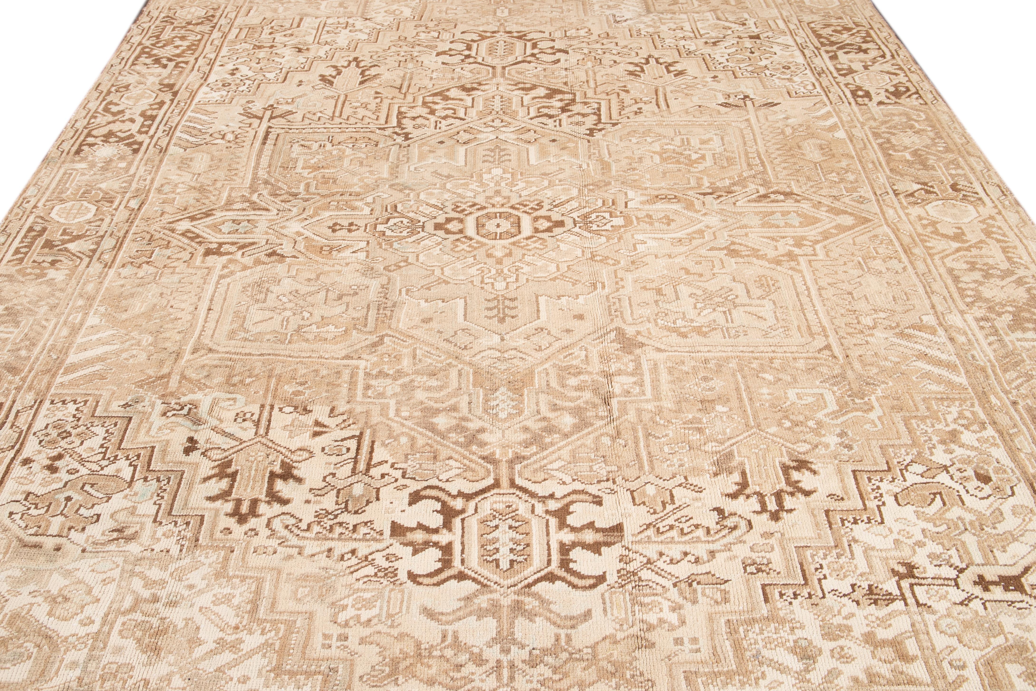 The antique Heriz rug showcases a refined and timeless elegance with its impressive all-over design and hand-knotted wool construction. The soft beige field acts as a backdrop to the eye-catching geometric floral pattern, adorned in shades of green