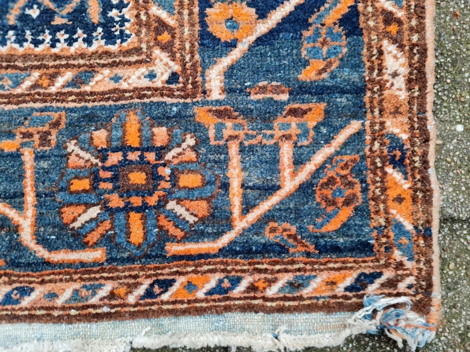 This striking antique Persian Malayer rug from the 1920s features a beautifully balanced geometric medallion design rendered in rich indigo blue, terracotta orange, and ivory tones. The central diamond medallion is surrounded by a field of
