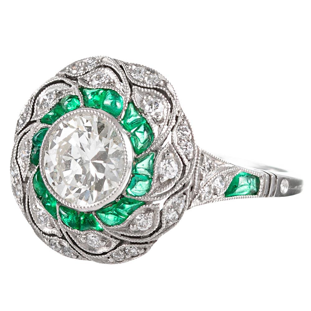 Detail abounds from every angle on this hand made platinum art deco inspired ring. With a .96 carat L/Vs2 diamond set in the center, the impact of the ring is augmented by an additional white diamonds and custom-cut emeralds. Note the filigree under