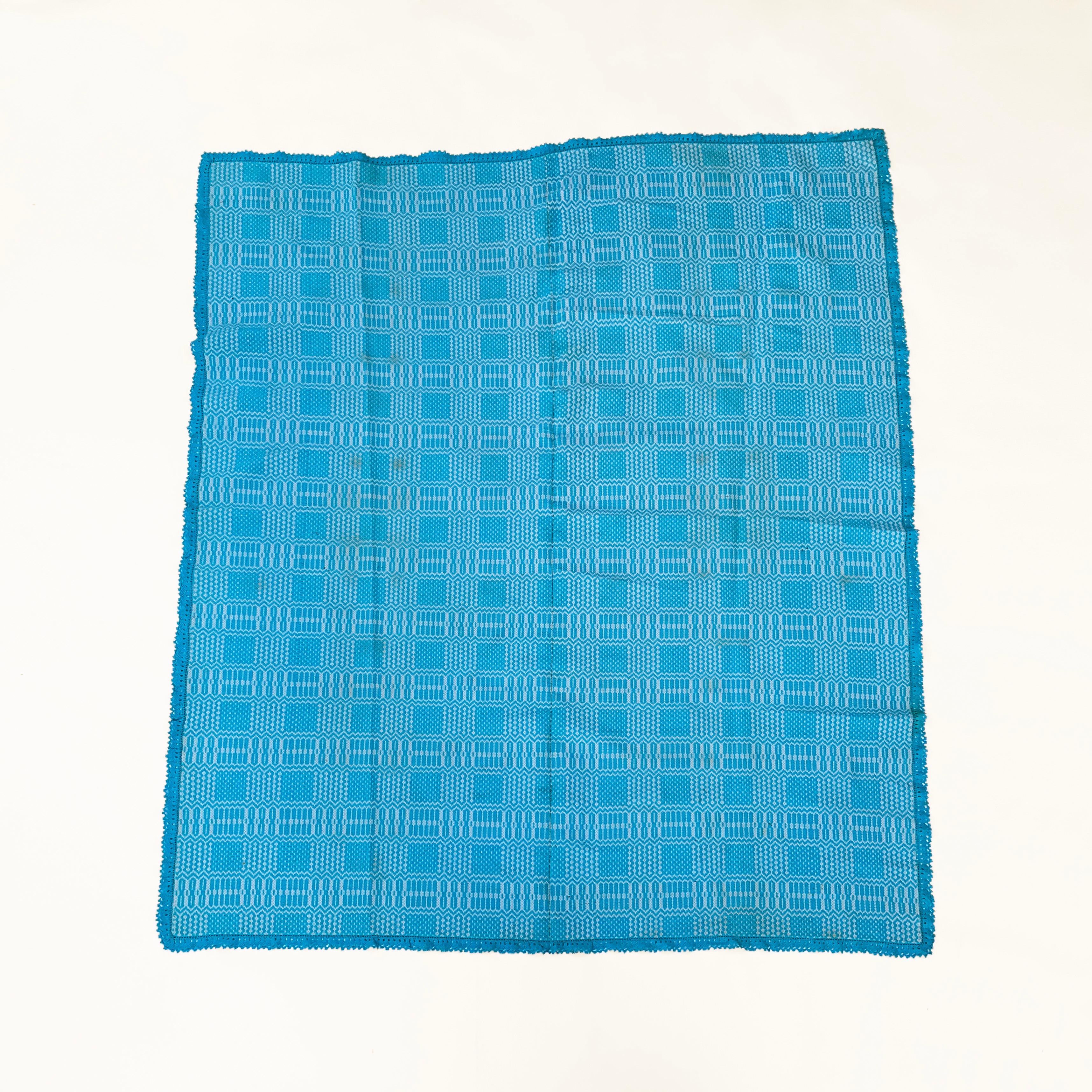 A large, baby blue blanket – that could be used as a throw, comforter, or piece of decorative wall art. This woven coverlet is made from a soft cotton and wool mix, and fits easily on a standard double bed. The piece was produced in the 1950s in