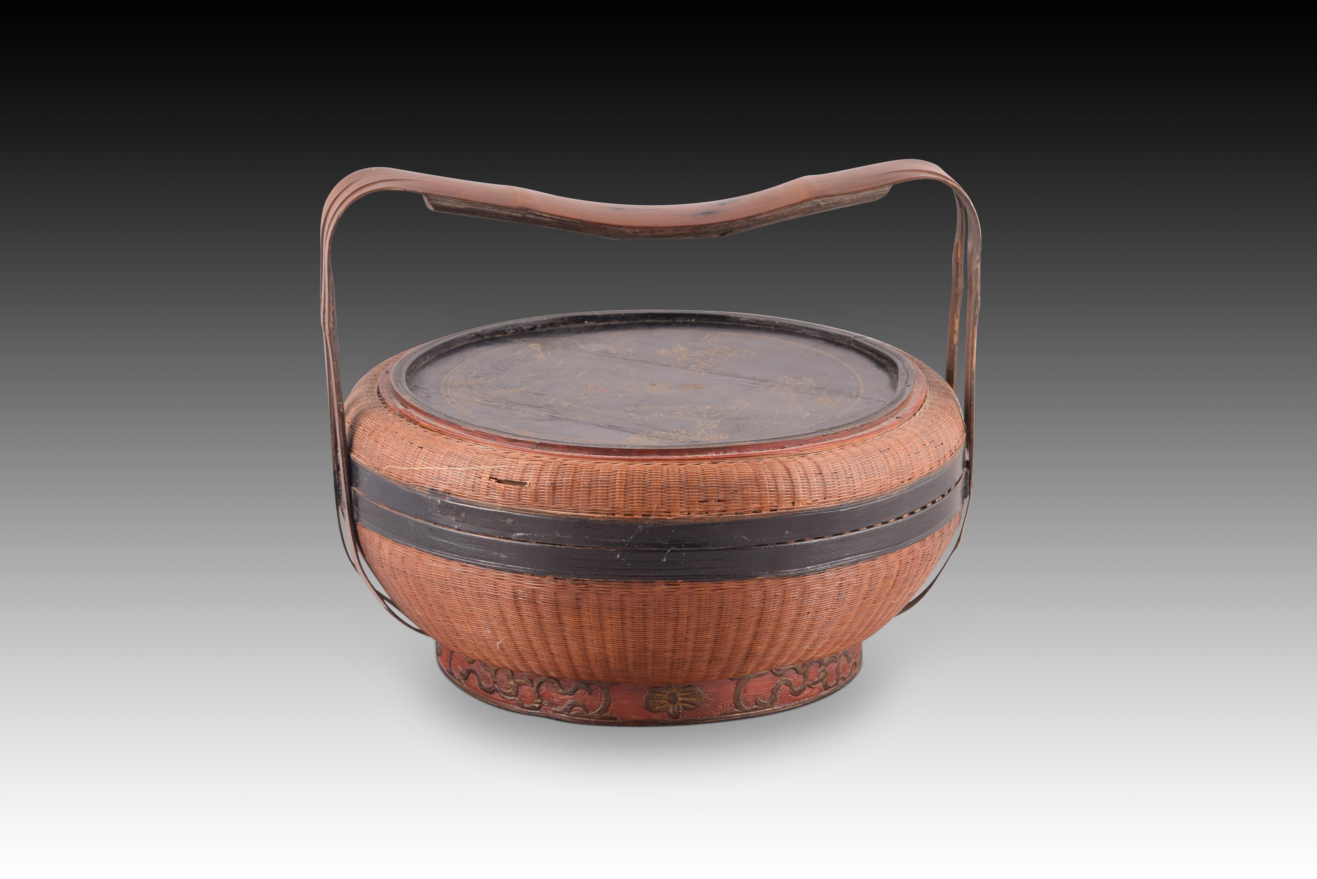 Handmade basket. Vegetable fiber and lacquered wood. China, towards the beginning of the 20th century.
 Chinese basket with a flattened ovoid shape that combines meticulous and complex basketry work on the body with lid, mouthpieces, handles and