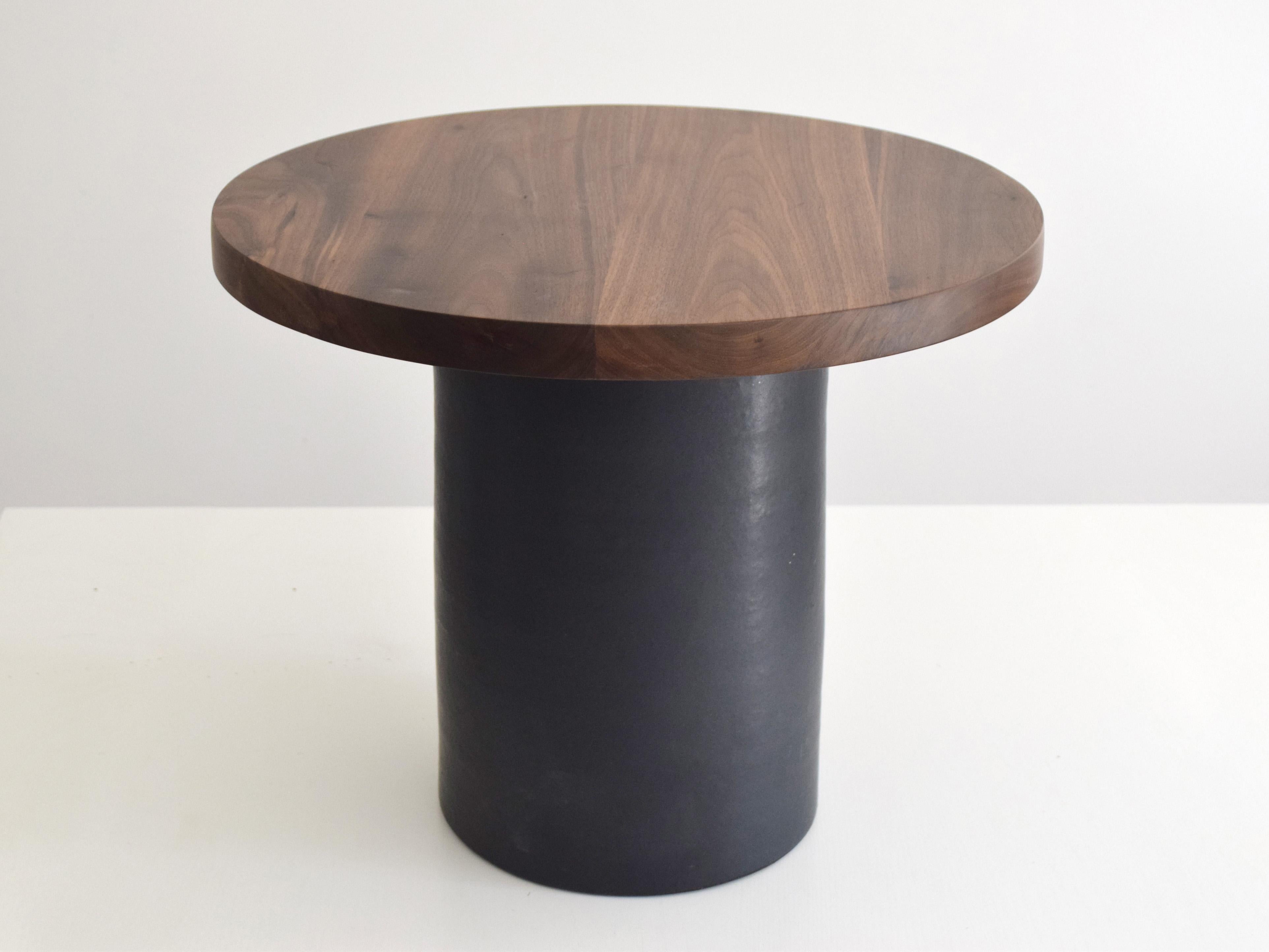 Questo tavolino artigianale combina una base scultorea in ceramica con un piano in noce massiccio, bilanciando l'artigianato con il design moderno. Progettato per essere utilizzato come tavolino o tavolino da caffè compatto, si adatta perfettamente