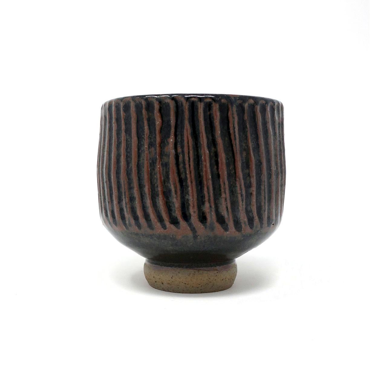A handmade ceramic vase with irregular stripes complemented by a small base that provides a gravity-defying effect. The glaze is black with warm brown lines. Signed 