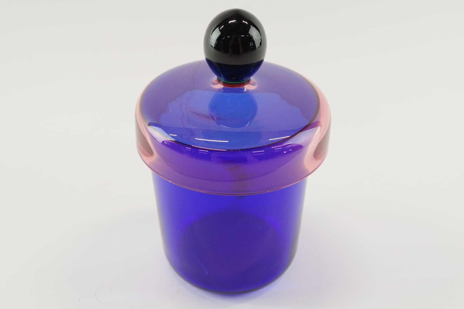 Questo vaso di vetro con coperchio, firmato dal famoso designer svedese Erik Höglund, è stato realizzato a mano nel 1992 presso la vetreria di Nový Bor, nella Repubblica Ceca. Questi barattoli sono diventati un oggetto da collezione. Il barattolo di