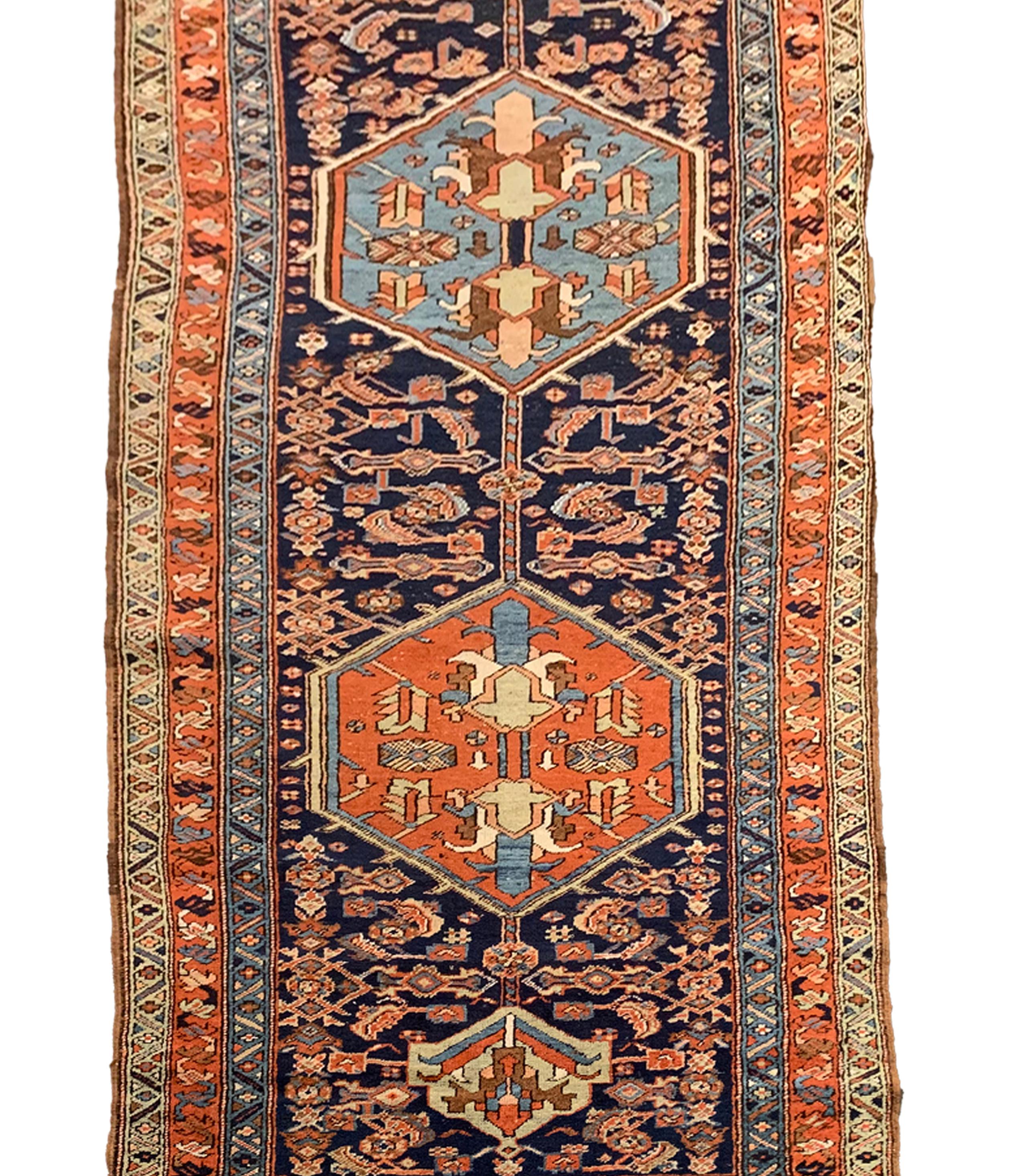 This antique rug runner fine wool runner rug is a handmade vintage piece featuring a tribal design. The central pattern features five geometric medallions woven in blue and rust accent colours with intricate details. The colour palette and tribal