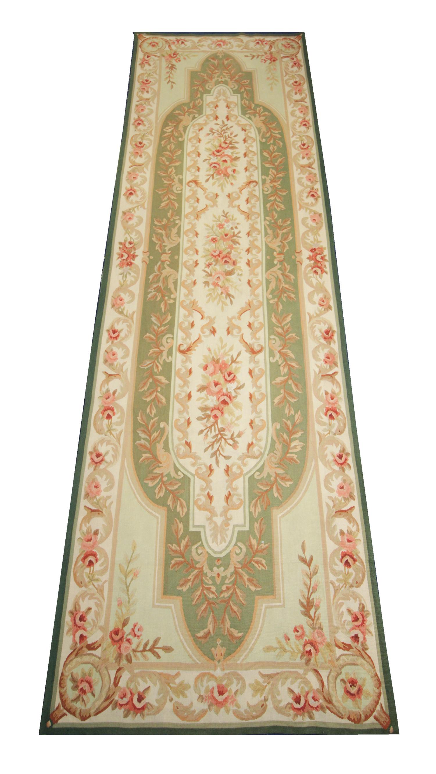 This handwoven Oriental needlepoint rug was woven runner by hand in China in the early 21st century. The central design features a symmetrical floral pattern woven with a unique color palette including green, cream, pink and beige. This fine