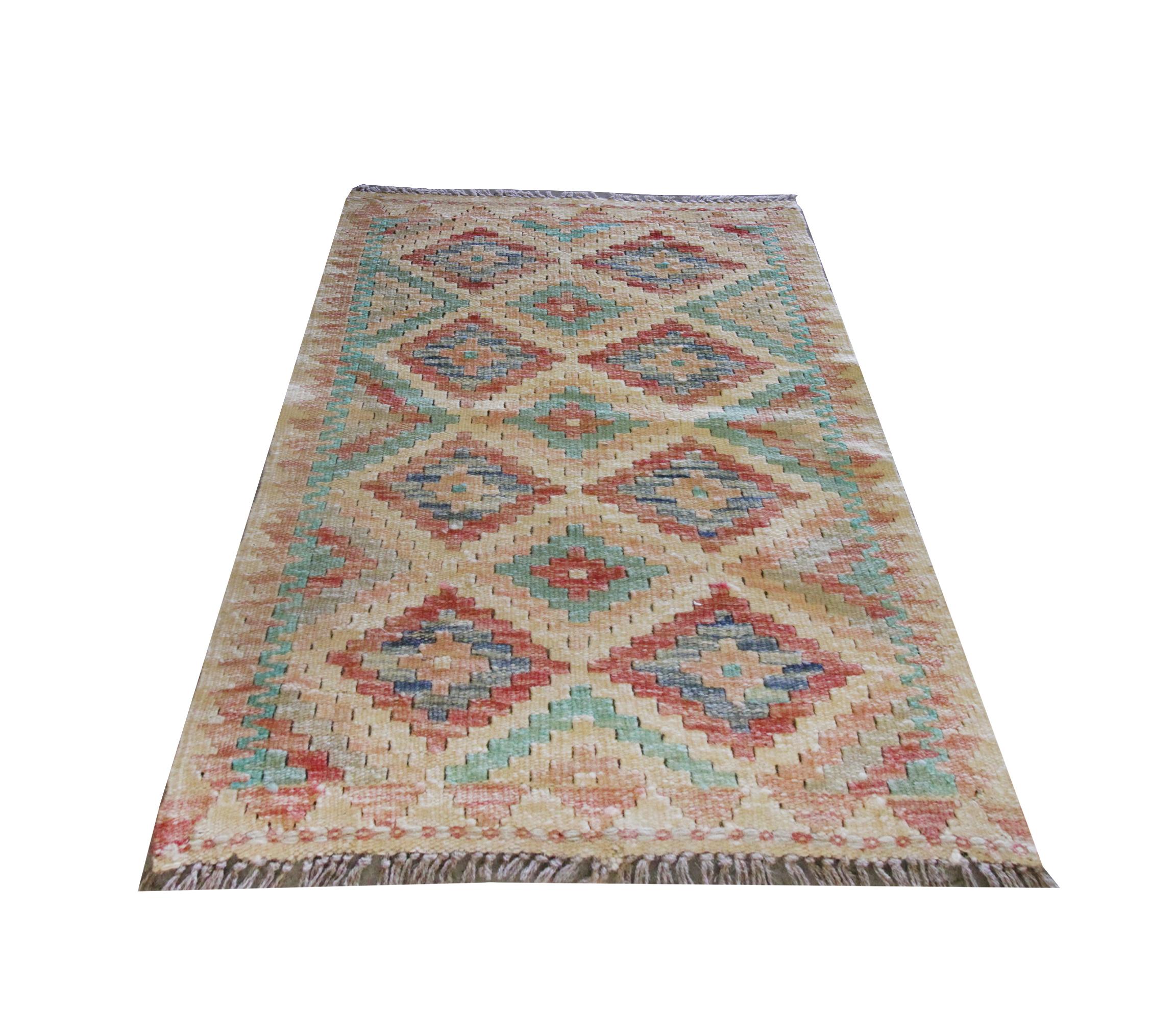 This small wool kilim is a handwoven area rug made in Afghanistan. The central pattern features symmetrical diamond motifs woven in red, blue, green and beige accent colours. This has then been framed by a repeating pattern border that encloses the