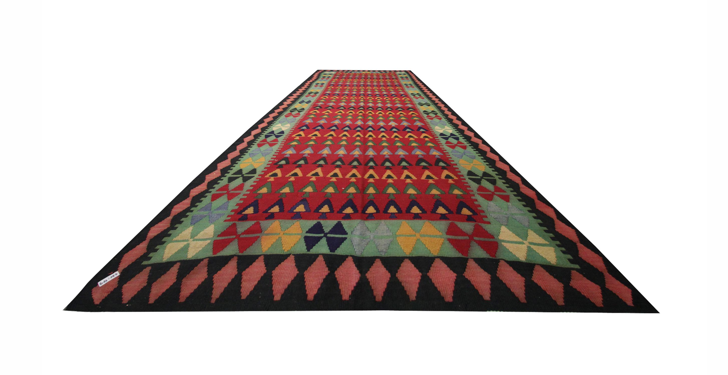 This fine wool handmade kilim was constructed in Azerbaijan in the 1960s/70s. The design features a rich red background with a bold repeating pattern in green, yellow, and blue accents. The central design has been framed with a repeating pattern