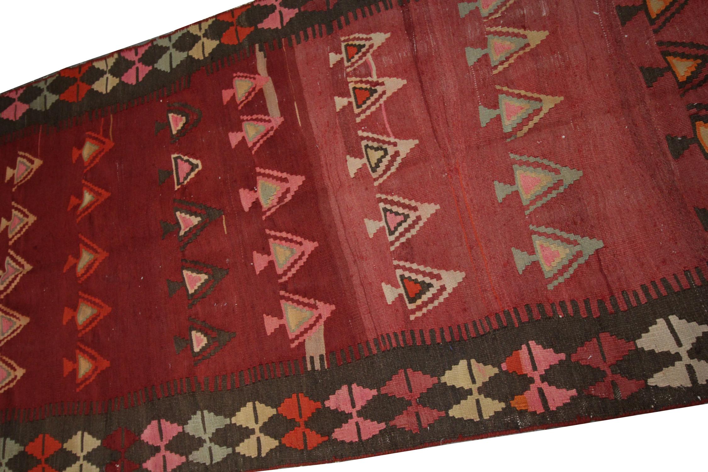 This fine wool handmade kilim was constructed in Azerbaijan in the 1960s/70s. The design features a rich red background with a bold repeating pattern in green, yellow, and blue accents. The central structure has been framed with a repeating pattern
