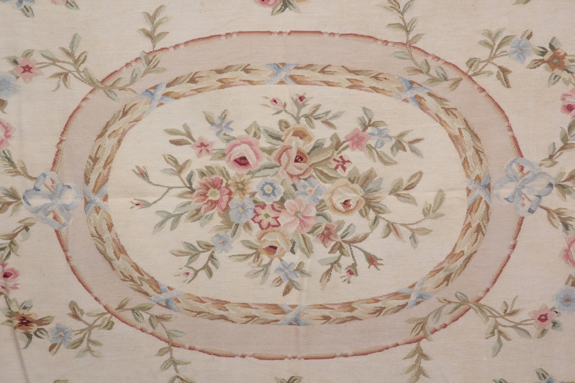 This handwoven needlepoint reveals delicate meandering floral designs woven on a cream background around the central medallion. The central design features a beautiful floral bouquet encapsulated in an oval. This is then enclosed by a