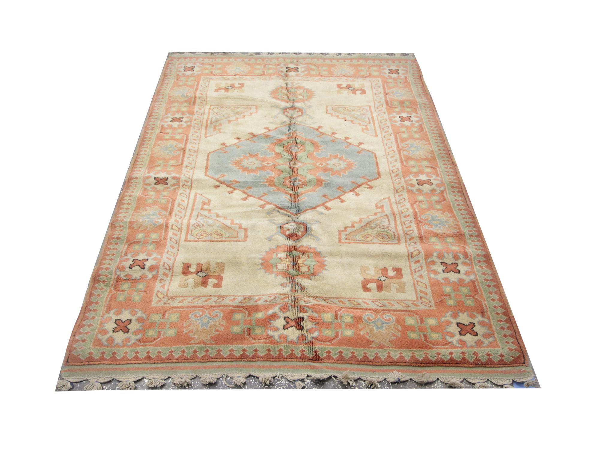 Pastel colorways cover this hand knotted vintage rug. Featuring a central medallion in the central design on a beige background. This is then enclosed by a highly-detailed orange and green border. This high-quality Turkish rug is perfect for both