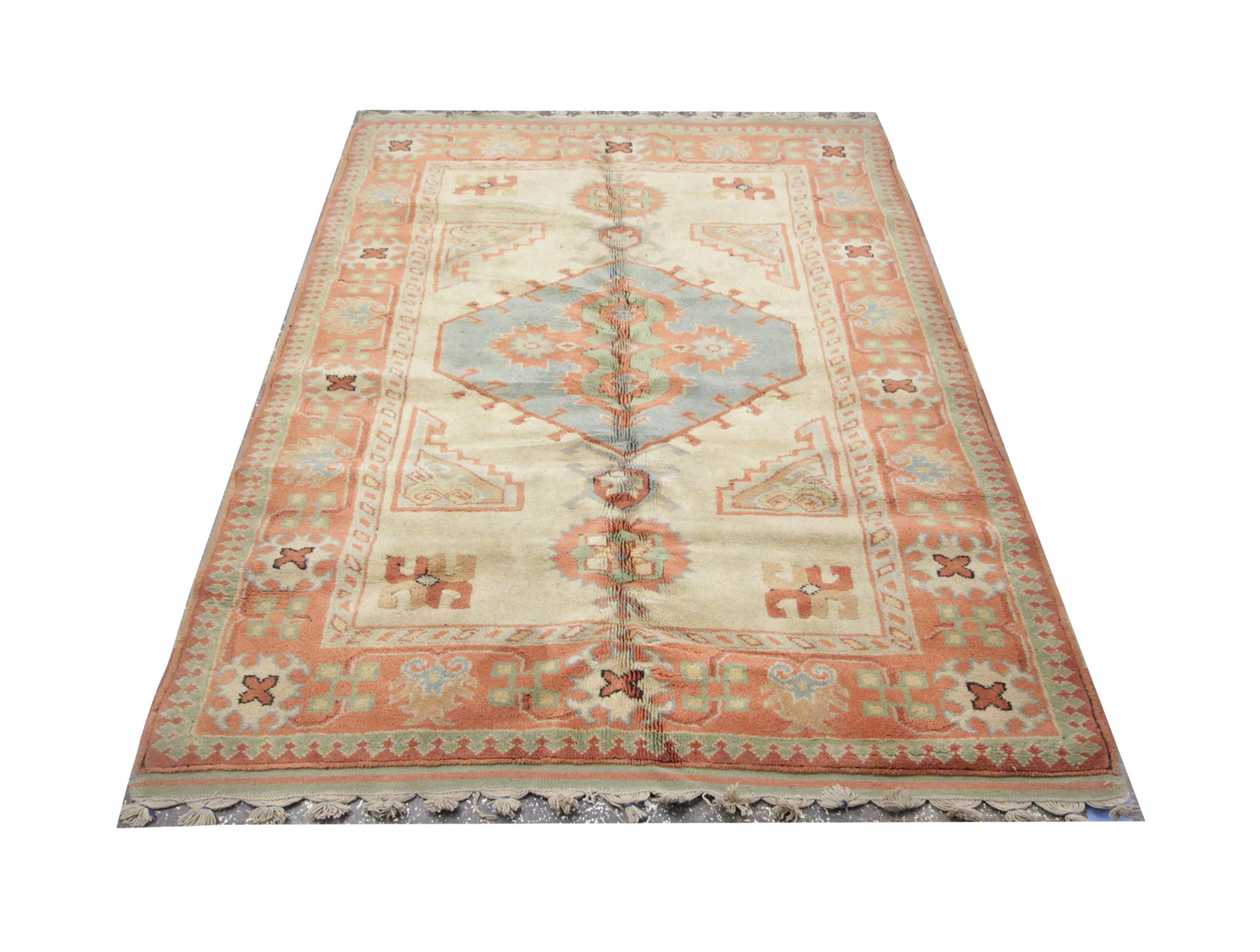 I colori pastello ricoprono questo tappeto vintage annodato a mano. Caratterizzato da un medaglione centrale su sfondo beige. Il tutto è racchiuso da un bordo arancione e verde molto dettagliato. Questo tappeto turco di alta qualità è perfetto per
