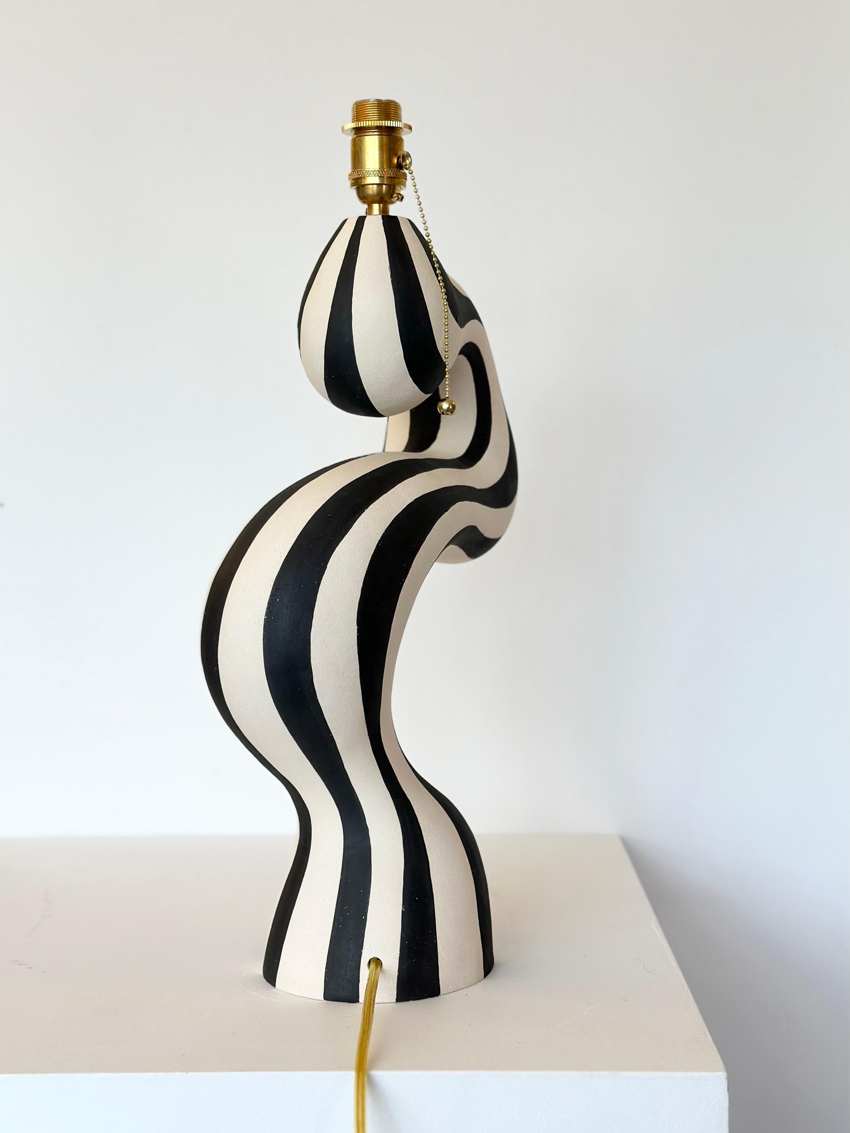 An art piece designed and handcrafted by ceramic artist Johanne Birkeland who works under the artist name Jossolini. The lamp base is hand built in white stoneware clay, and hand decorated with black matte glaze. 

The lamp comes with North American