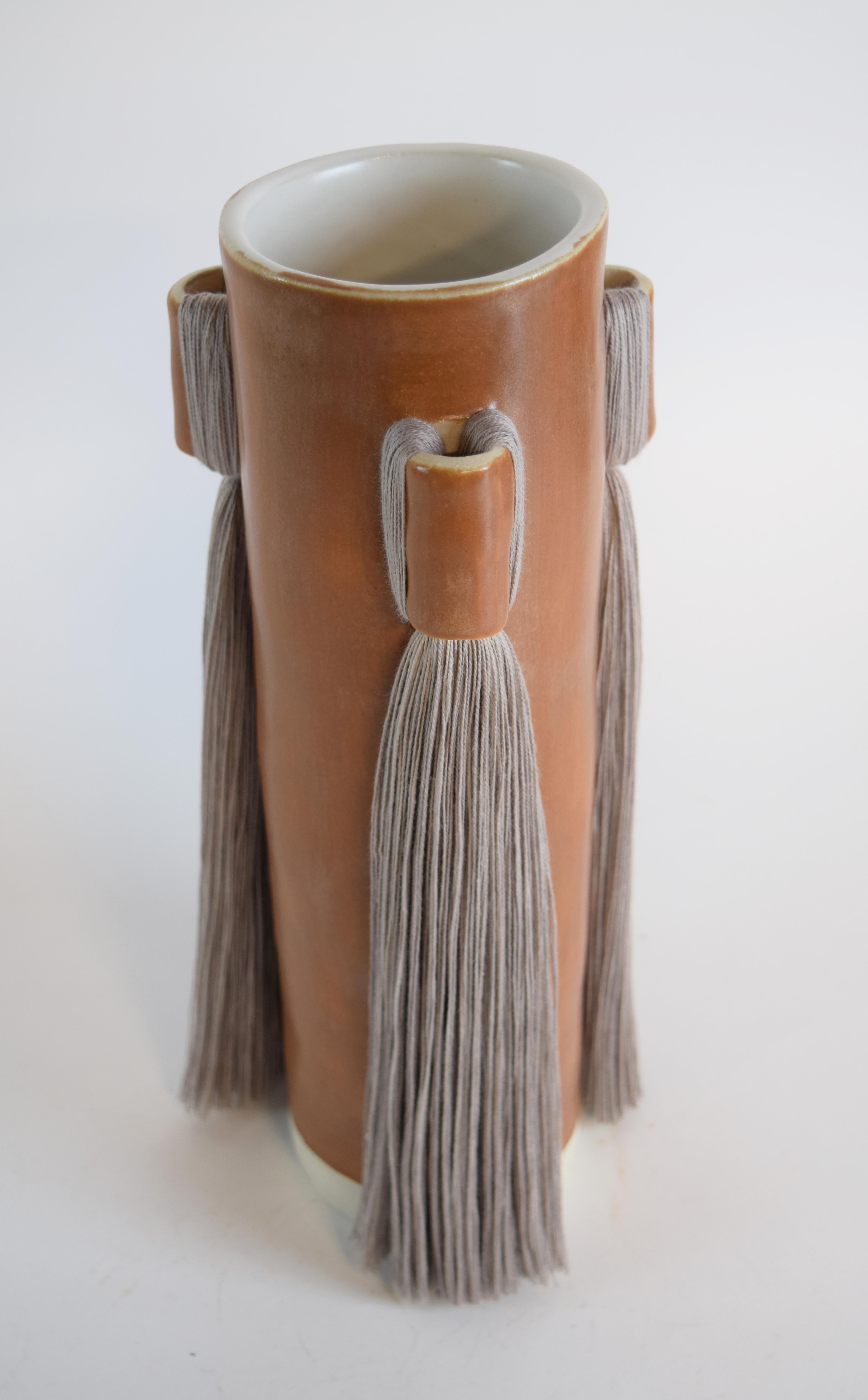 Vase #607 by Karen Gayle Tinney

Lengths of fringe adorn 3 sides of this vase which is sized generously to hold a large arrangement of flowers.

Hand formed stoneware with satin brown glaze. Light gray cotton fringe detail. Inside is glazed white,