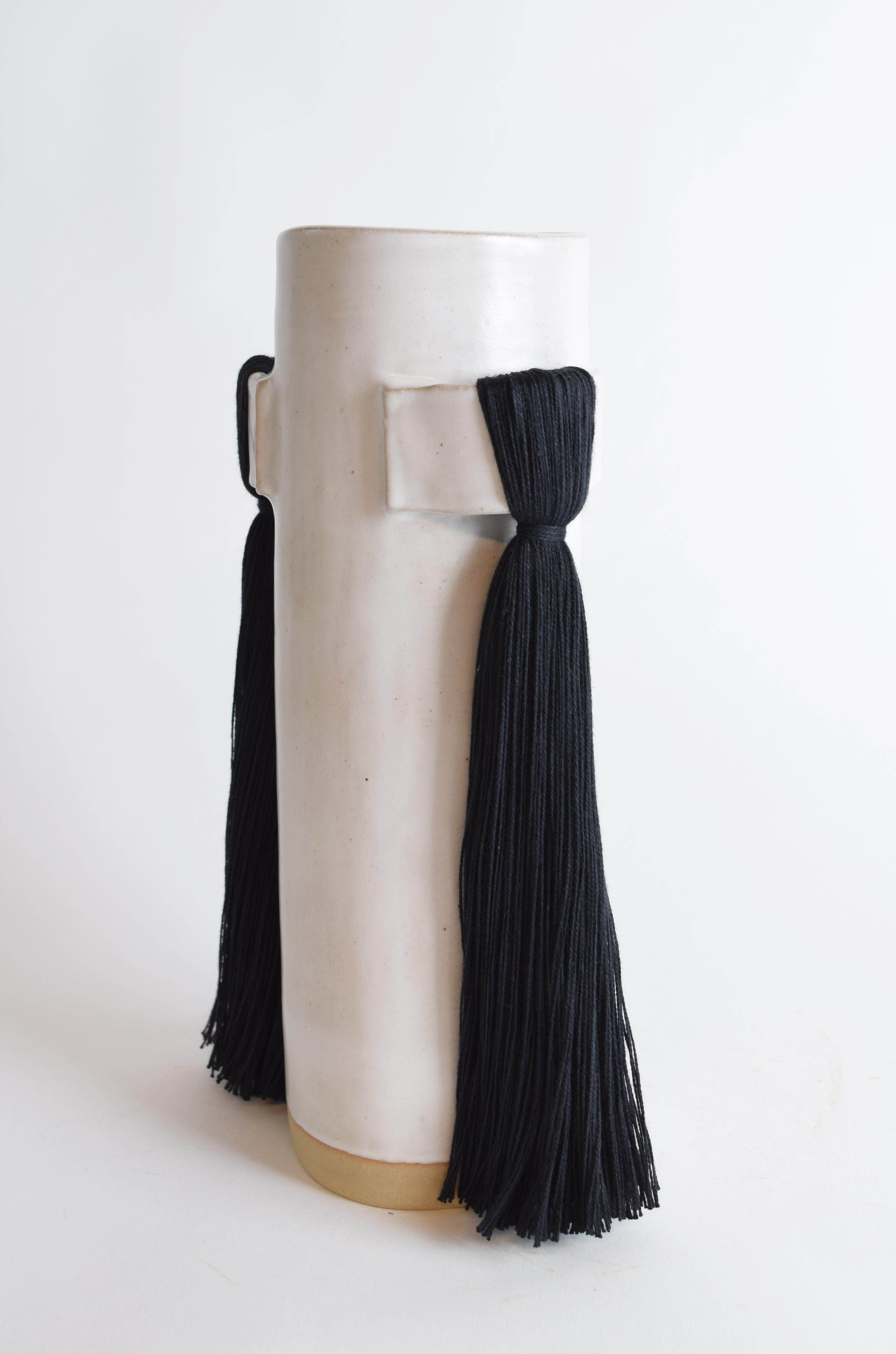 Vase #825 by Karen Gayle Tinney

A petite vase perfectly sized to stand alone in a small space or act as a companion to a larger piece. 

Stoneware with satin white glaze. Black cotton fringe detail. Inside is glazed white, the vessel can hold