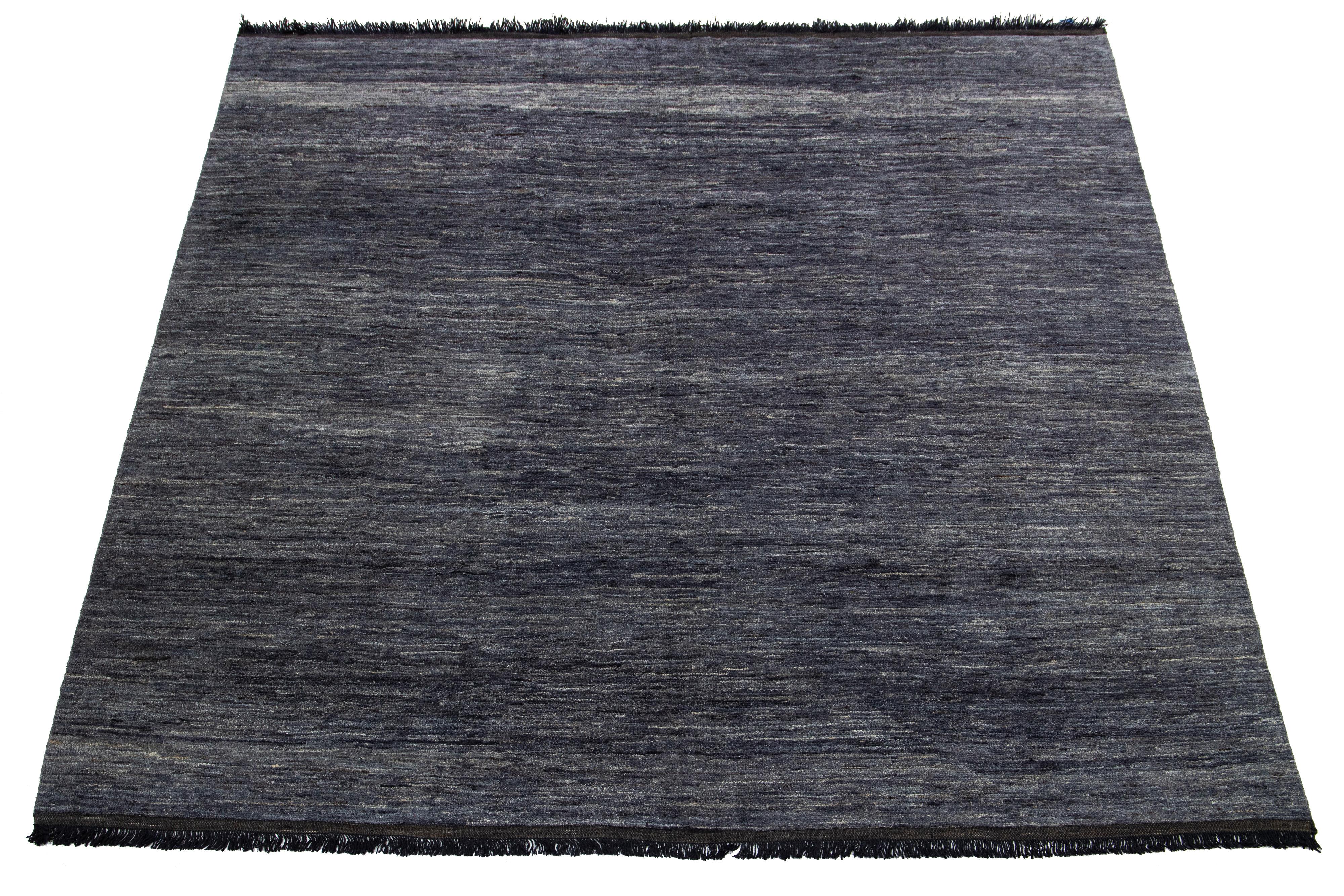This handcrafted wool rug, designed in the Gabbeh style, features a solid design highlighted by black fringes and a gray-charcoal background.

This rug measures 8'3