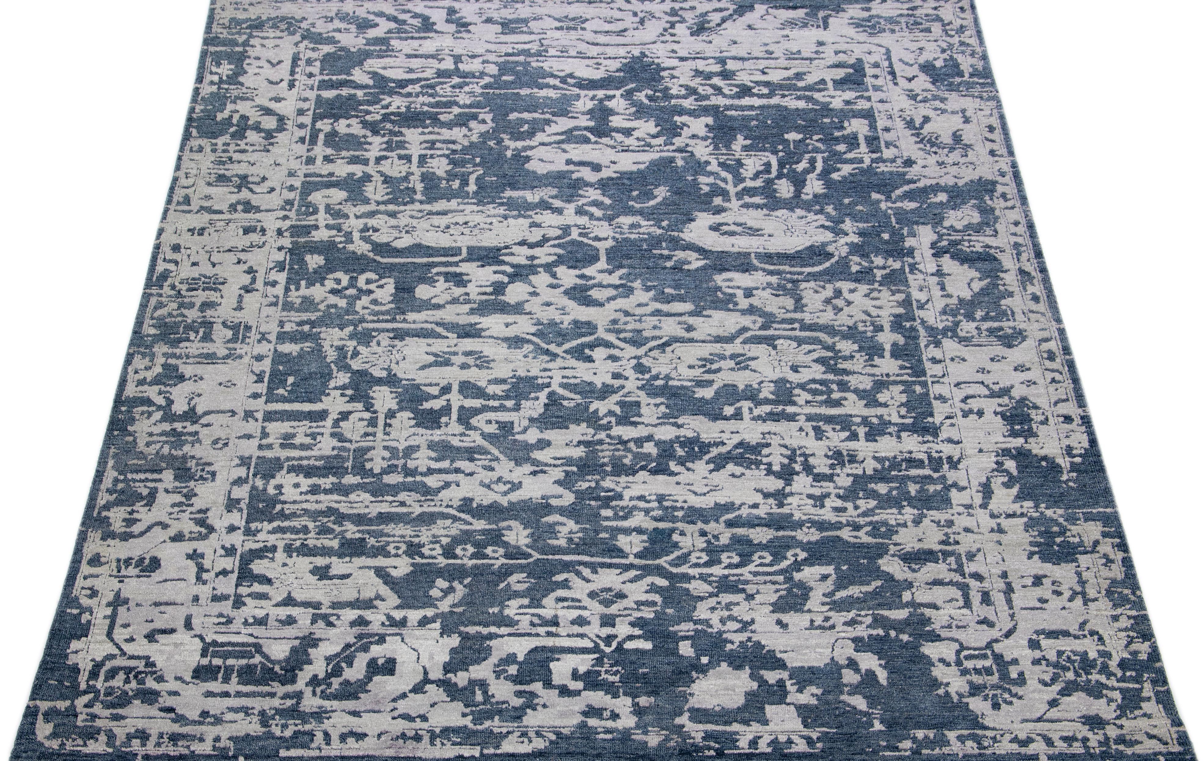 This stunning, modern Indian wool and silk combination rug is both elegant and stylish, featuring a navy blue field amidst an abstract patterning of gray. Its combination of luxurious wool and silk fibers offers a comfortable softness, while its low