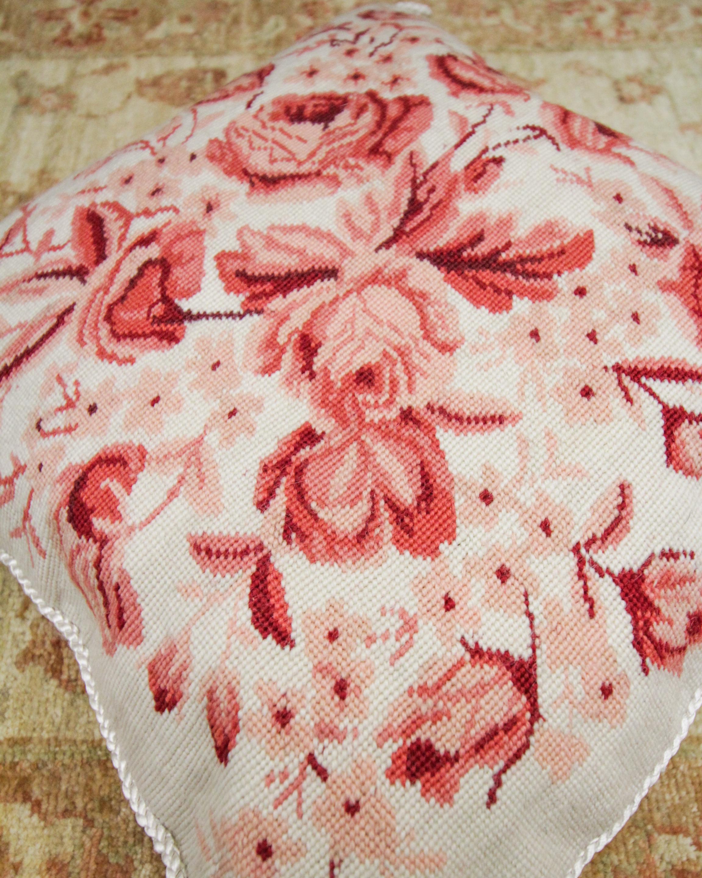 This floral hand needlepoint cushion cover is an excellent example of vintage cushion covers woven in the 1990s. The floral pattern has been woven in rich red and pink tones on a subtle cream background, detailed with a rope edge and corner design.