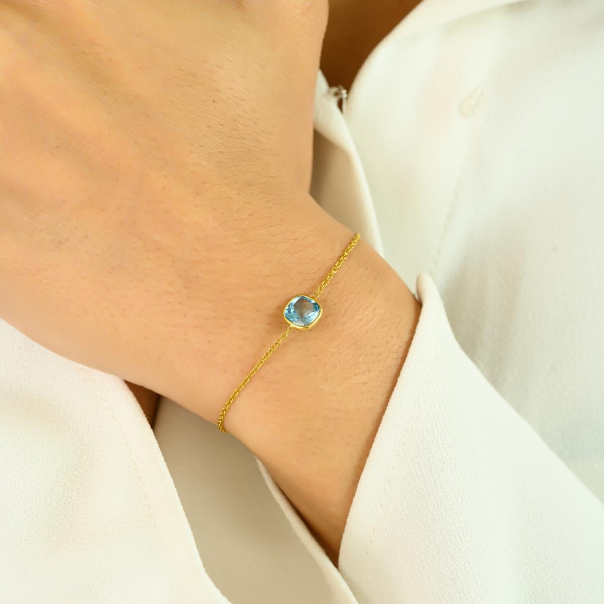 Esta elegante pulsera de oro amarillo de 14 quilates tiene una brillante piedra azul talla cojín de 1,4 quilates como radiante pieza central. Engarzada en una fina cadena de oro, la vibrante tonalidad de la piedra contrasta maravillosamente con el