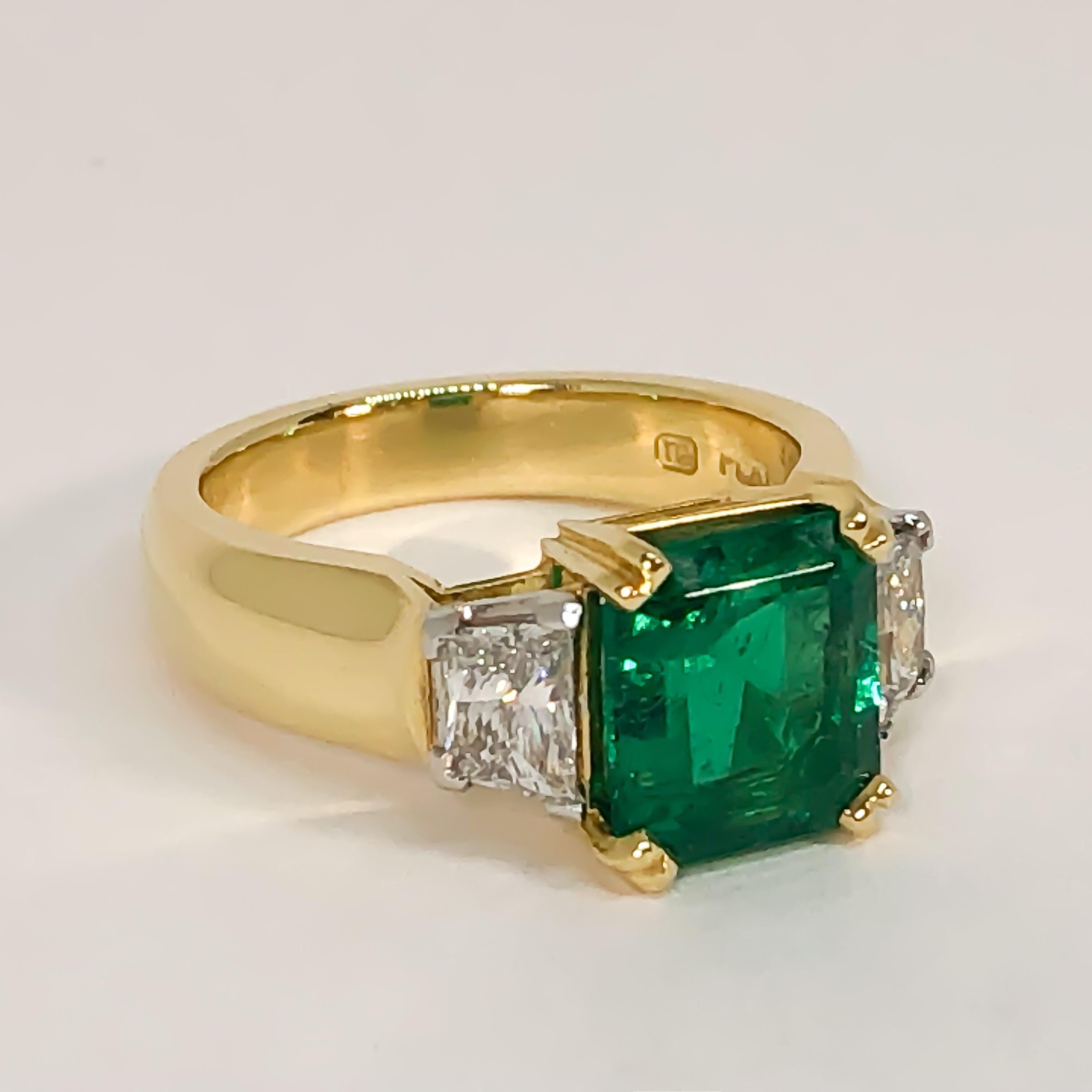 Natural Colombian emerald and diamond ring designed and handmade by Mark Areias Jewelers. Fashioned from 18 karat yellow gold and platinum and set with a stunning fine quality natural emerald, flanked by two trapezoid diamonds. The emerald is set in