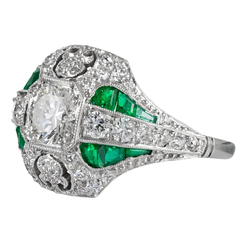 An impressive creation that will not go unnoticed, the center is set with a .79 carat (L/Vs) brilliant diamond. Framed by an intricately-embellished diamond and emerald border, the major stone sits low to the finger, where it is protected and can be