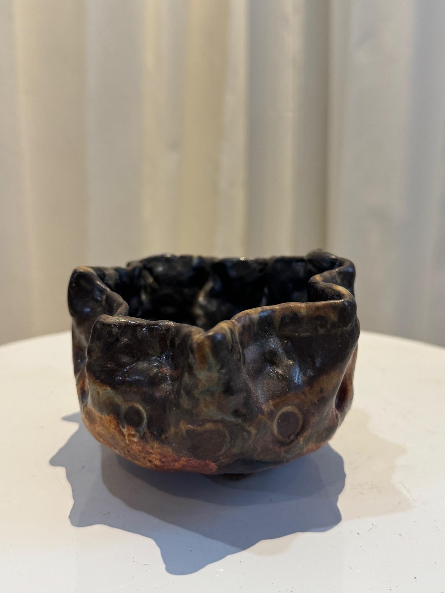 Ce vase en céramique de forme libre fait à la main est un exemple frappant de poterie organique et sculpturale, incarnant la beauté de l'imperfection grâce à sa forme brute et expressive. Son bord asymétrique et ondulé et sa surface texturée créent
