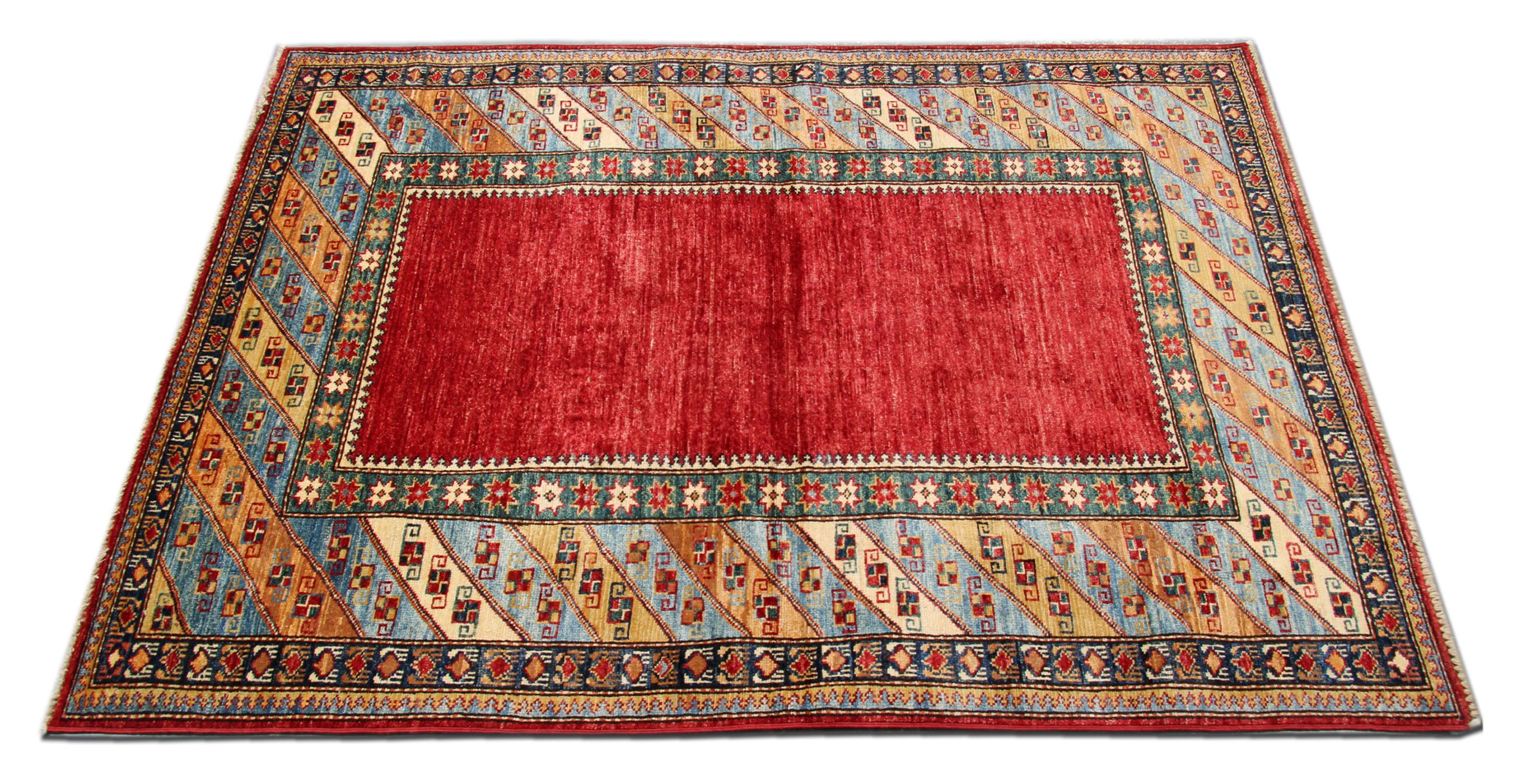 A beautiful new traditional Afghan Kazak rug features a conventional tribal minimal design woven in red, beige, blue and green accents through the centre on a red field. The design is then finished with a highly-detailed repeat pattern border that