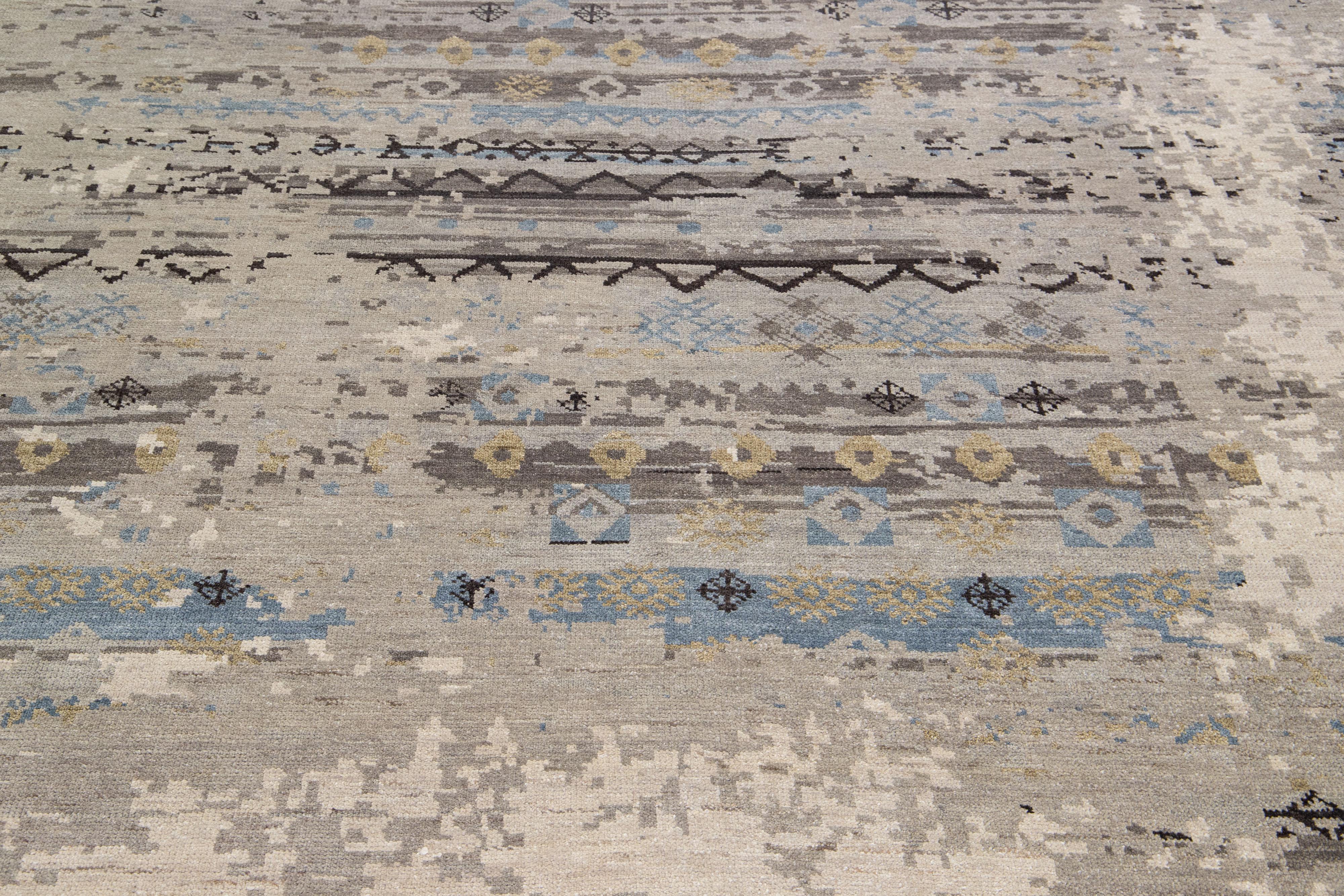 Dieser Teppich aus Wolle und Seide besticht durch sein modernes Design mit einem fesselnden Tribal-Motiv in einem eleganten Grauton. Die exquisiten blauen und hellbraunen Akzente ergänzen das ausgeprägte abstrakte Muster perfekt und verleihen ihm