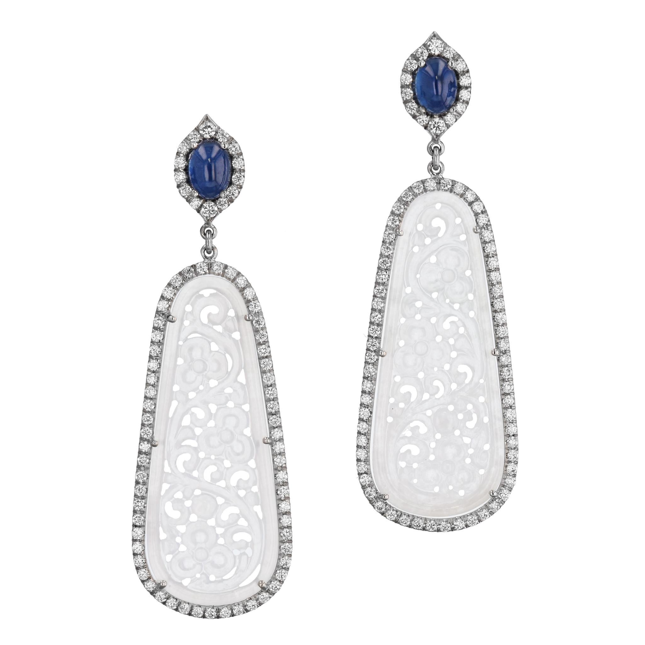 These stunning one of a kind, handcrafted icy jadeite earrings feature captivating 38 mm x 15 mm oblong carved oval jadeites and stunning cabochon sapphires set in diamonds pave halos. 
These magnificent 18 karat white gold drop earrings are a true
