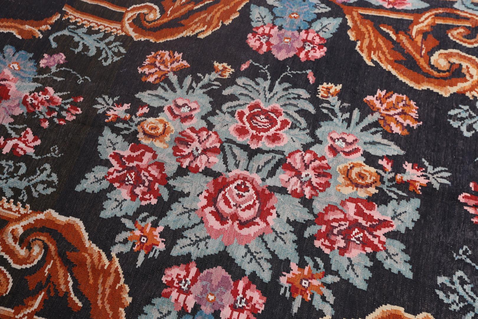 This luxurious antique floral rug is a Moldavian Kilim woven by hand in the 1940s. Elegantly woven roses flow through this design, woven symmetrically to create a beautiful, eye-catching display. Featuring a deep brown background with green, yellow,