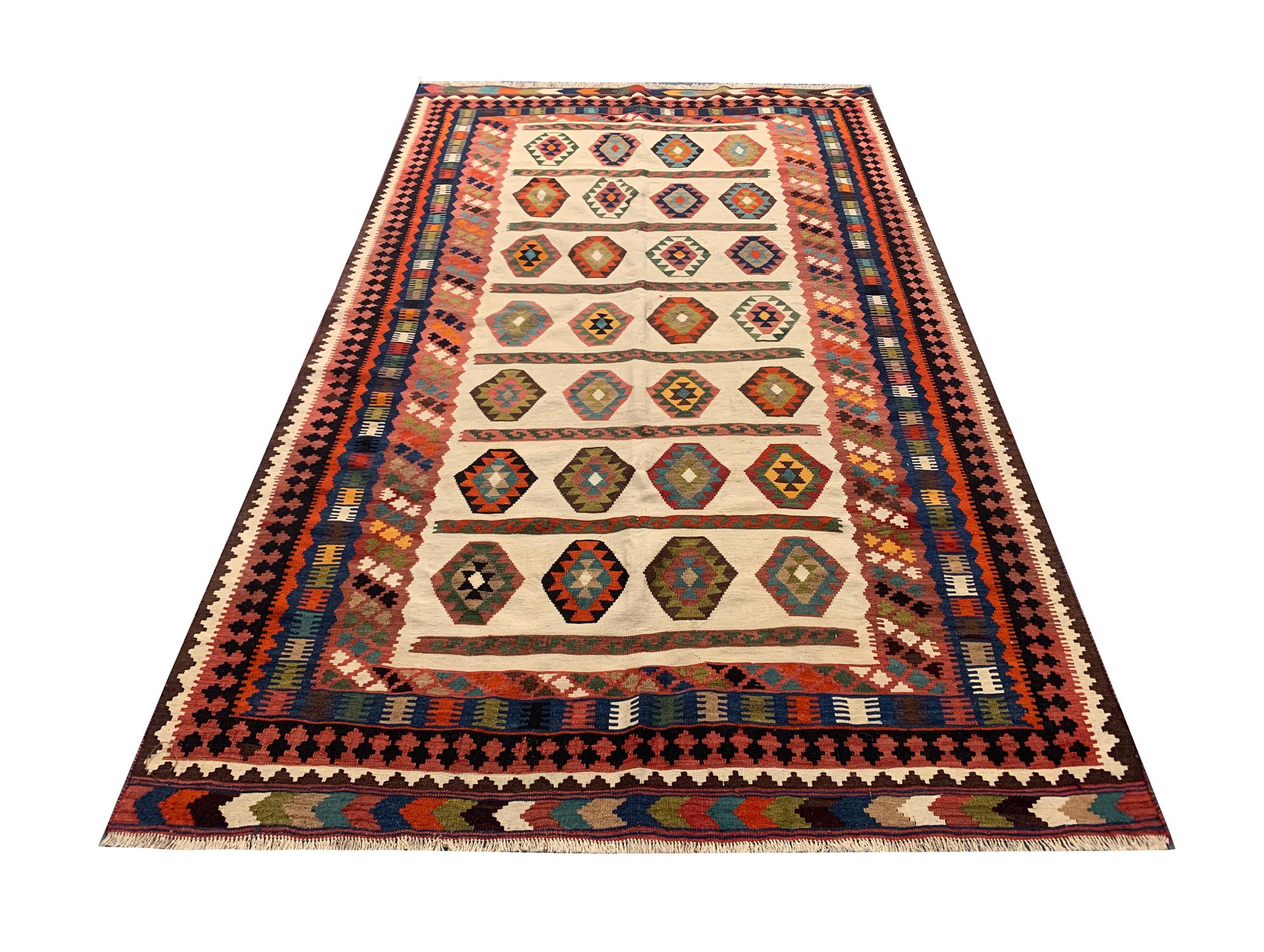 This fine wool rug has featured a bold geometric tribal motif design in accents of green, pink, orange and blue with a cream background and a thick layered border made up of repeat patterns. Both the colour palette and design of this wool rug are